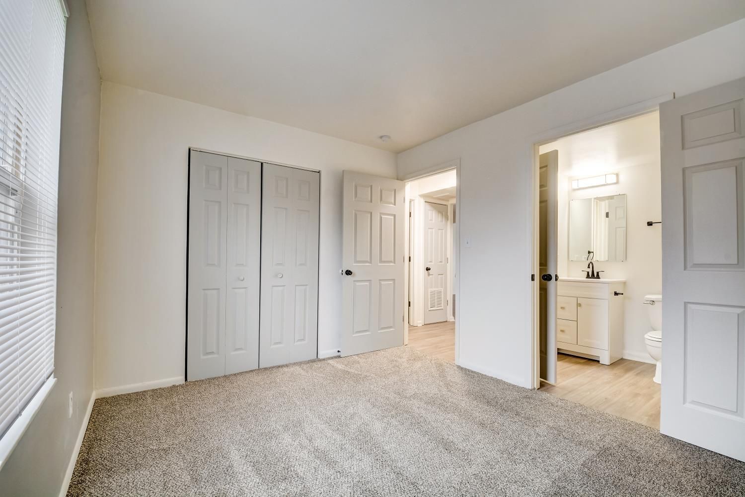 An empty bedroom with a bathroom , closet , and window.