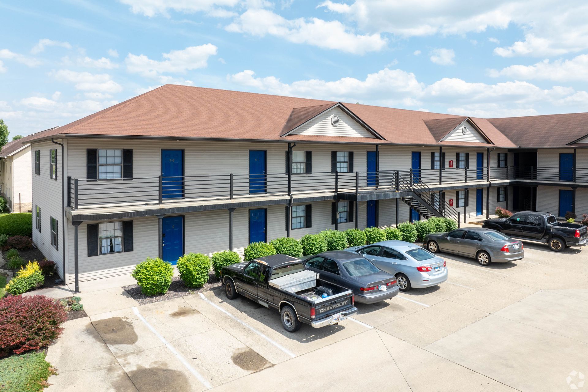 A row of cars are parked in front of a large apartment building.