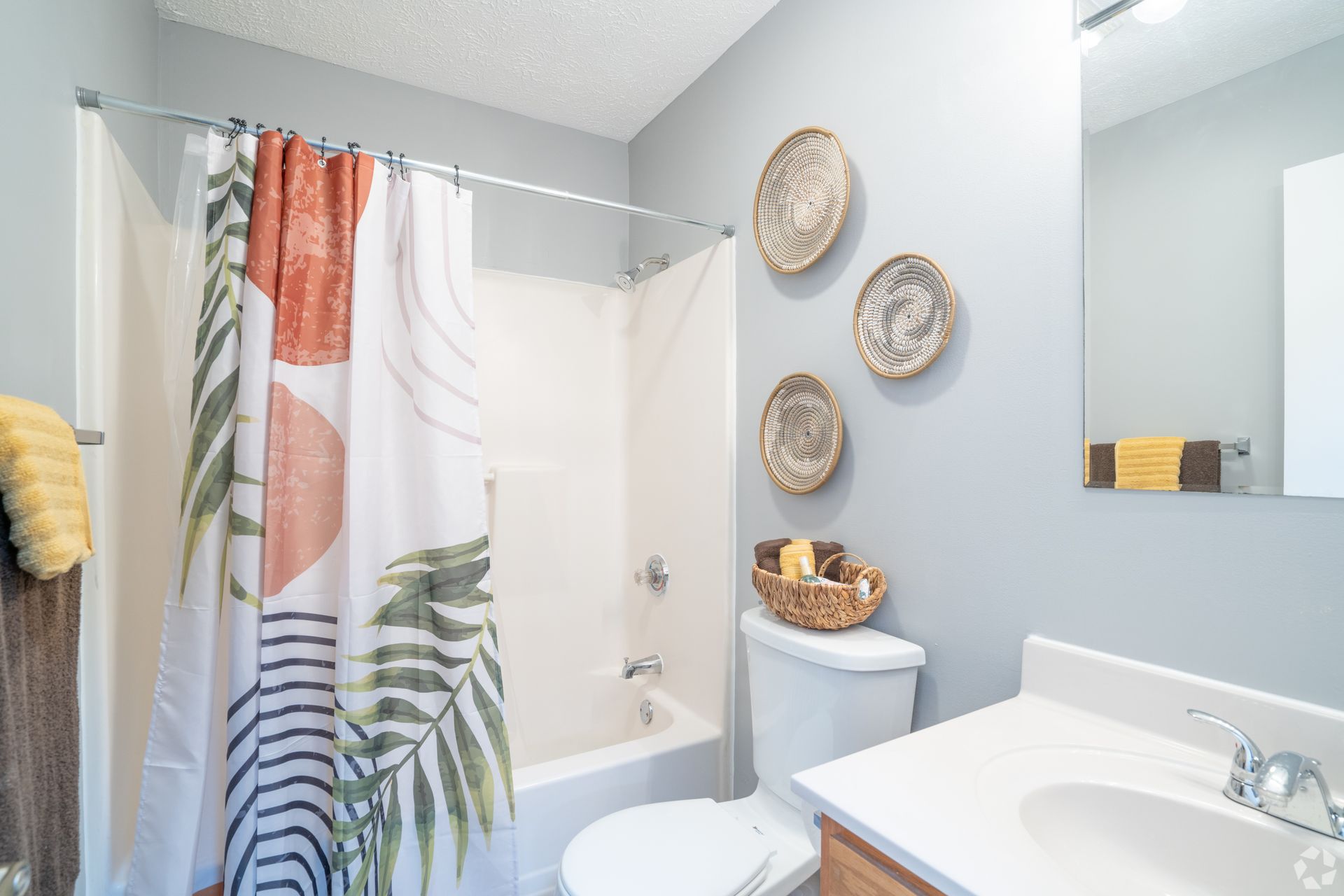 A bathroom with a shower curtain , toilet , sink and mirror.