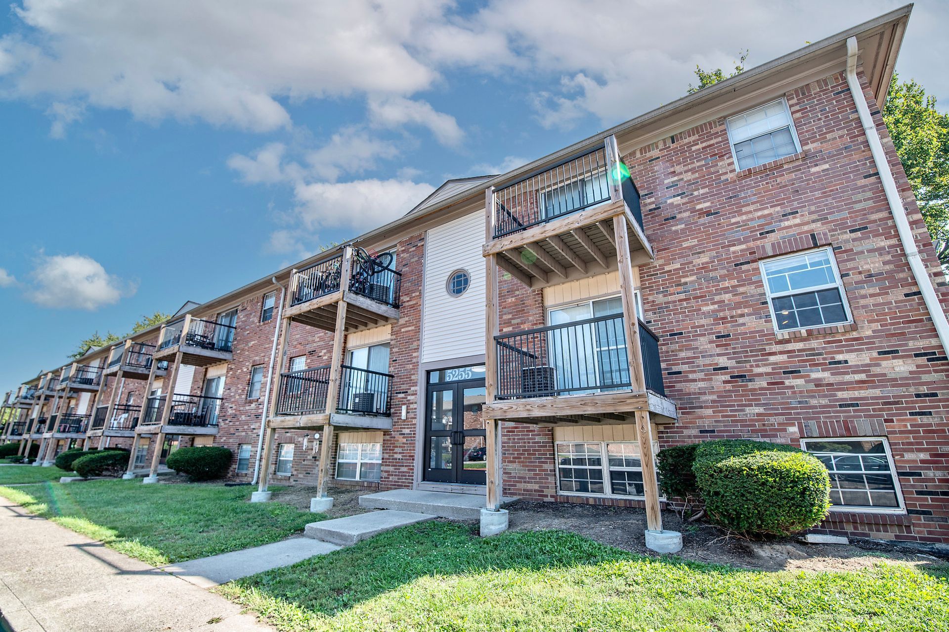 A large brick apartment building with balconies and a blue sky in the background.