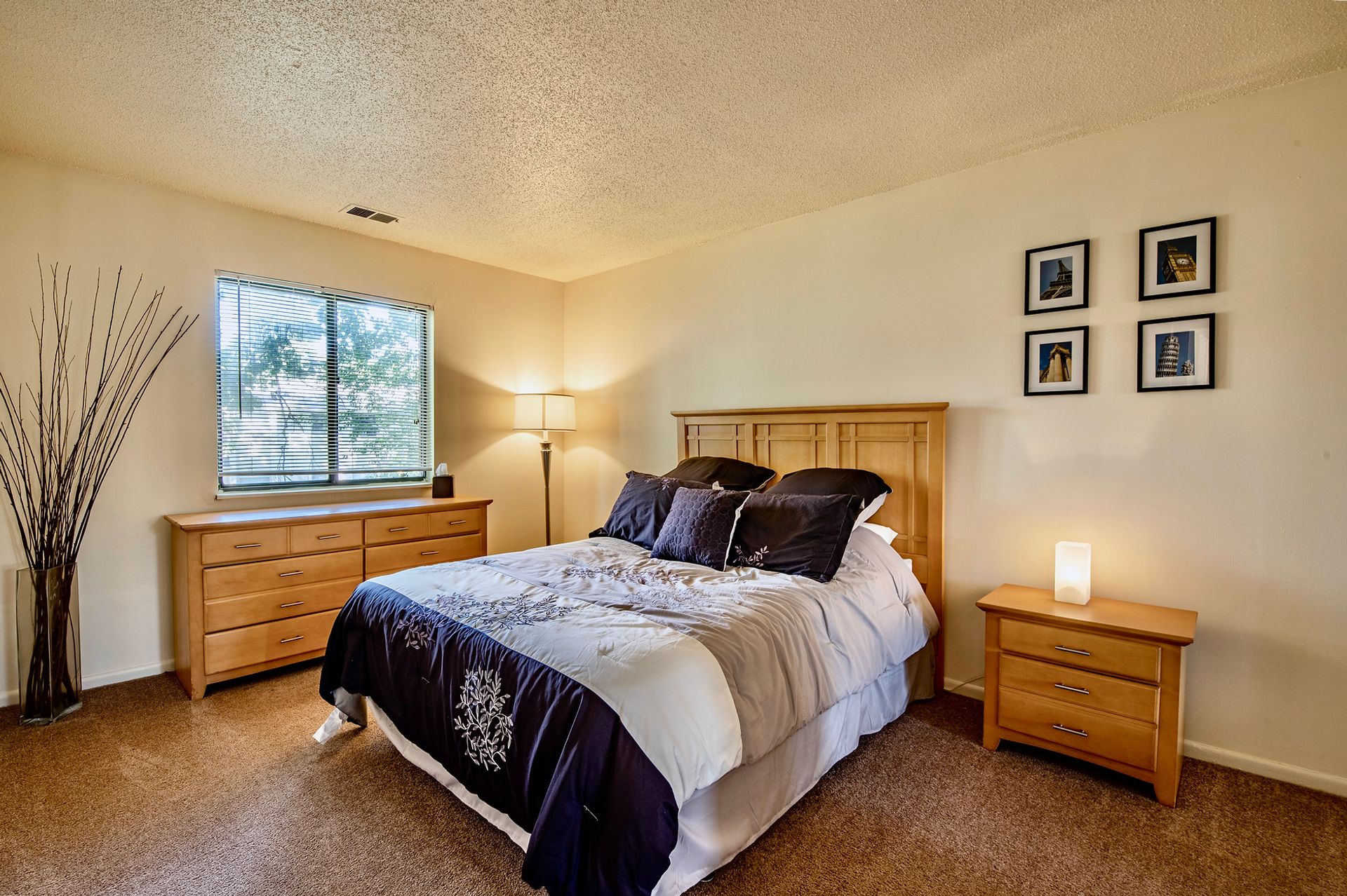 A bedroom with a bed , nightstand , dresser and window
