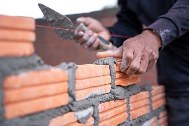 Bricklayer using a trowel to apply mortar on a brick wall, red bricks, hands, outside.
