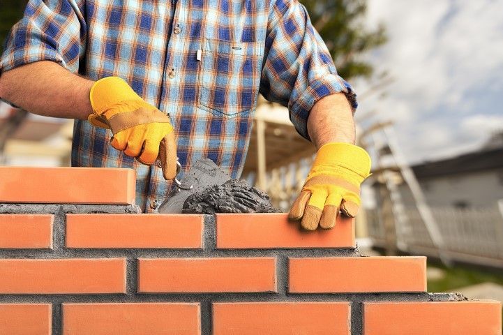 Person laying bricks, wearing yellow gloves, outdoors.
