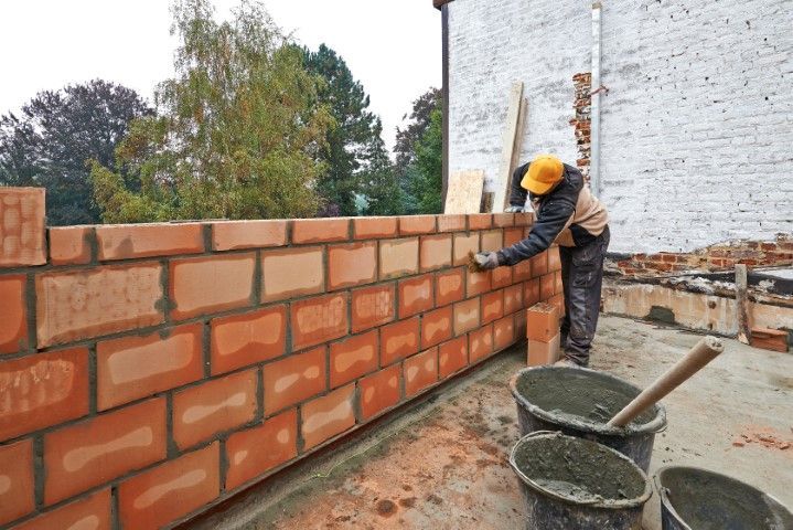 Construction worker building a red brick wall, applying mortar, outdoors.