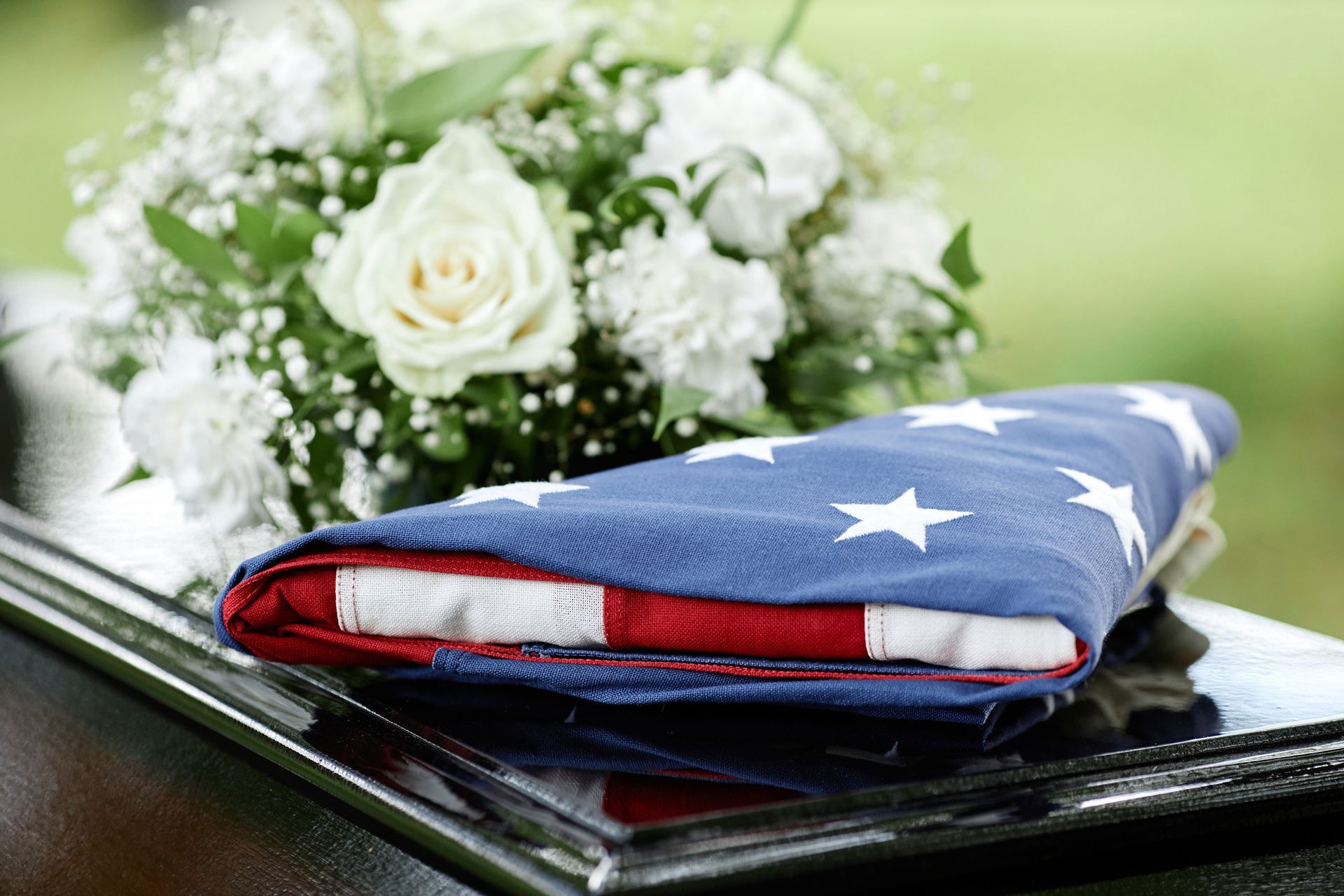 An american flag is laying on top of a coffin next to a bouquet of flowers.