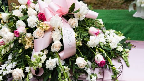 A pink coffin decorated with white flowers and a pink bow