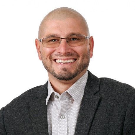 A man wearing glasses and a suit is smiling for the camera