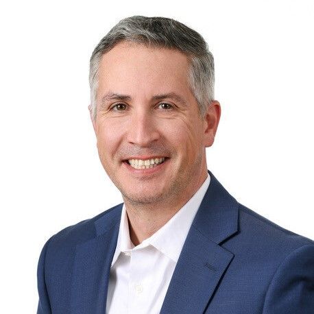 A man in a blue suit and white shirt is smiling for the camera.