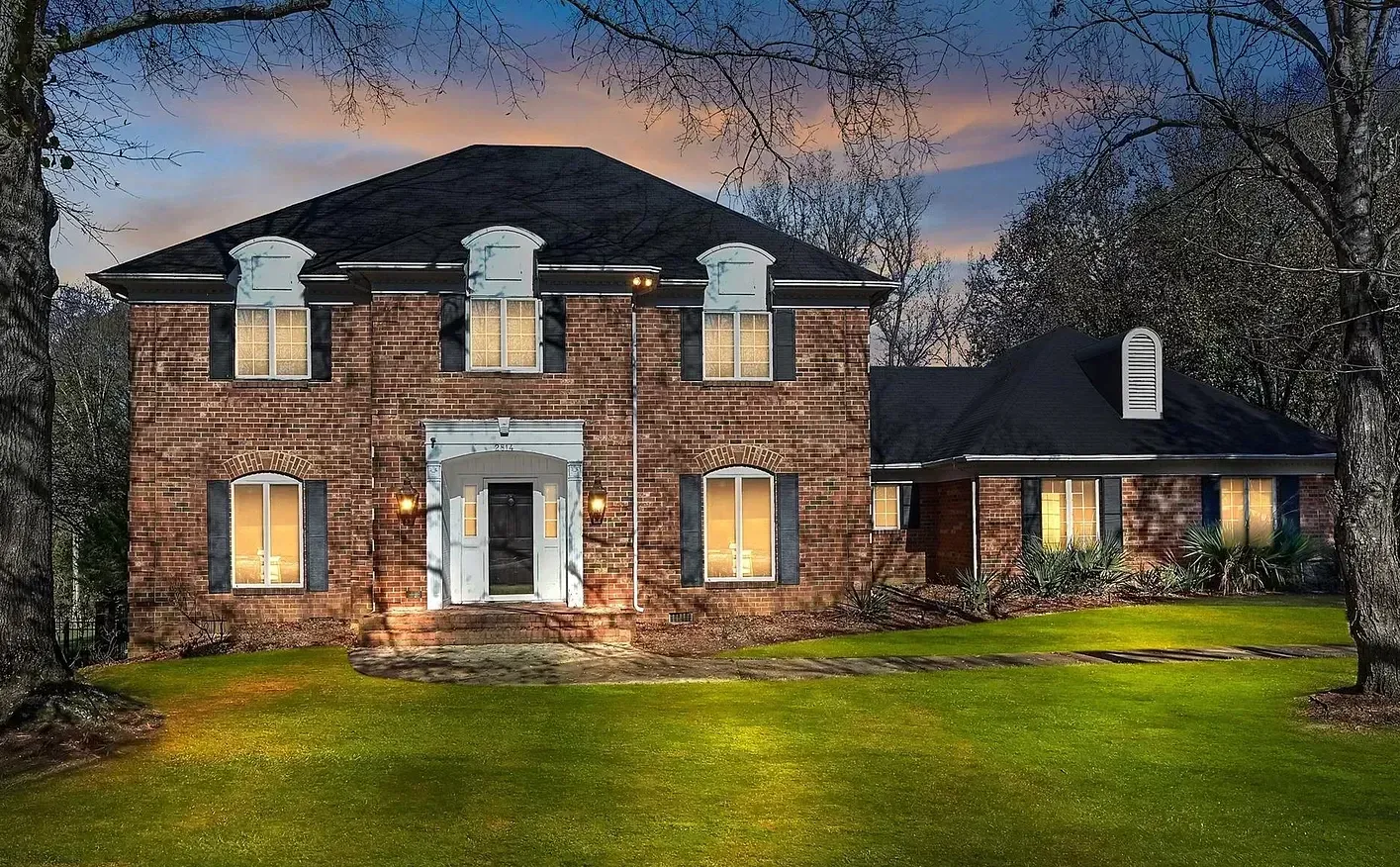 A large brick house with a black roof is lit up at night
