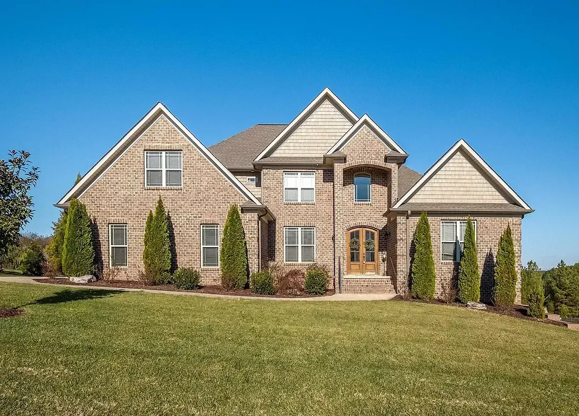A large brick house sits in the middle of a lush green field