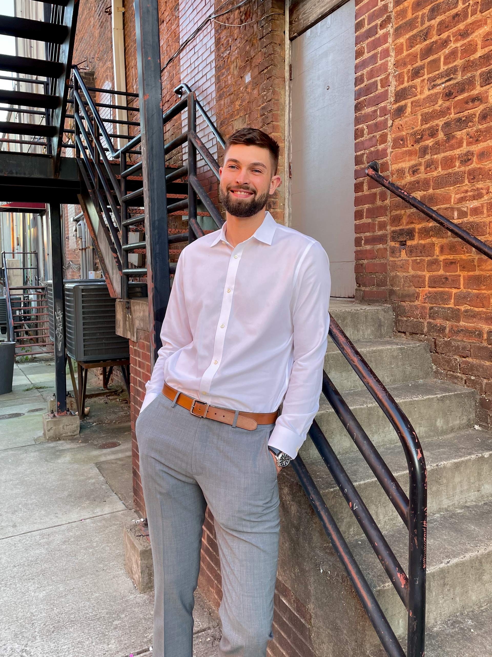 A man in a white shirt and grey pants is leaning against a railing