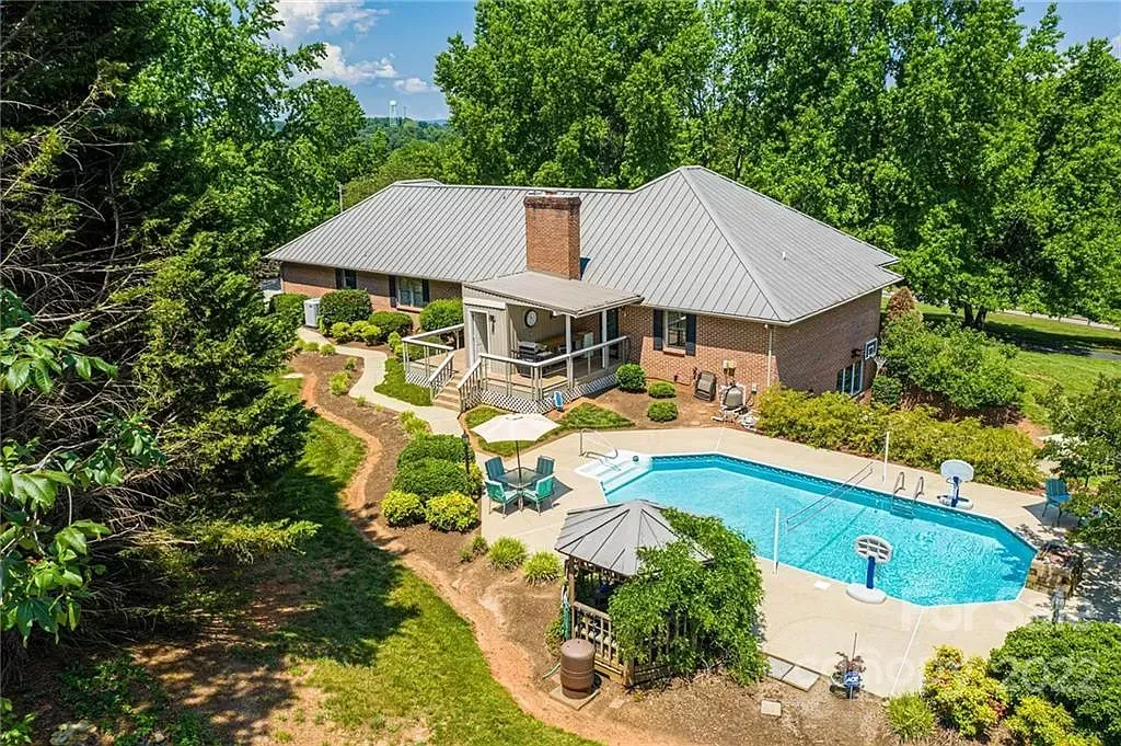An aerial view of a house with a large swimming pool surrounded by trees.