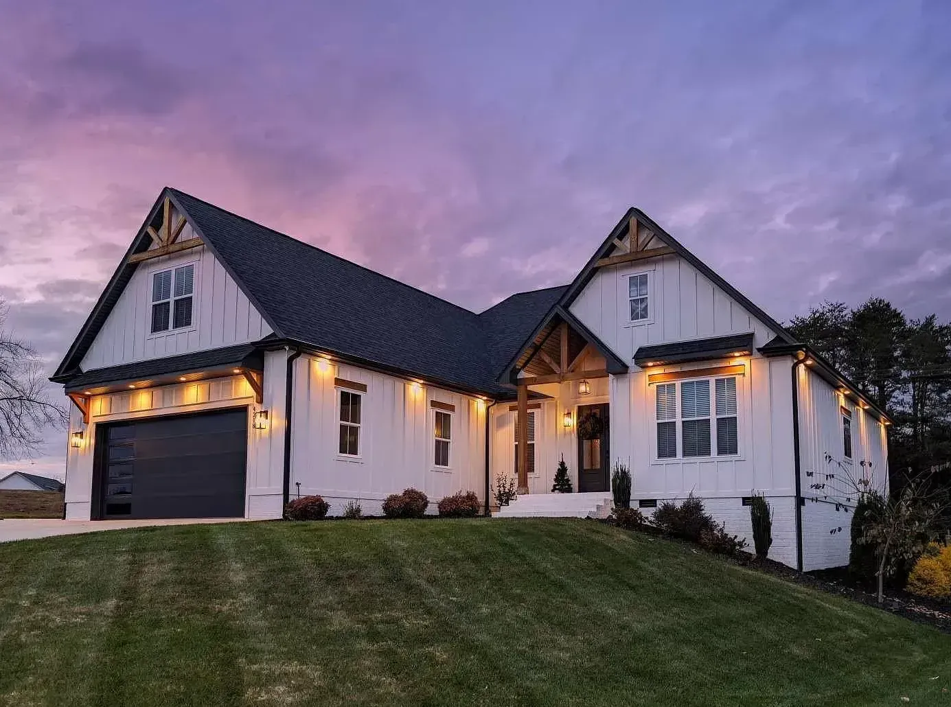 A white house with a black garage door is sitting on top of a lush green hill.