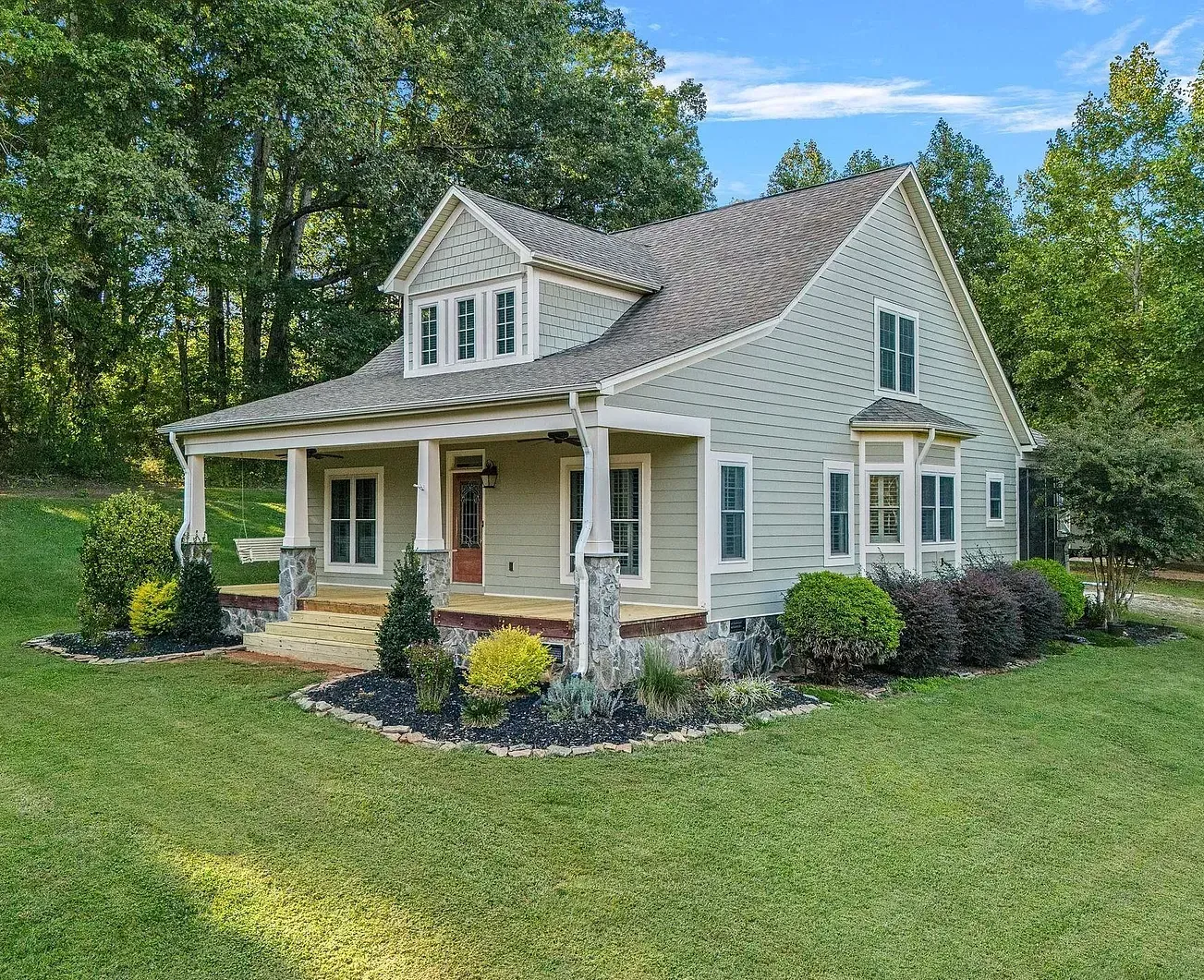 A small house with a porch is sitting on top of a lush green field.