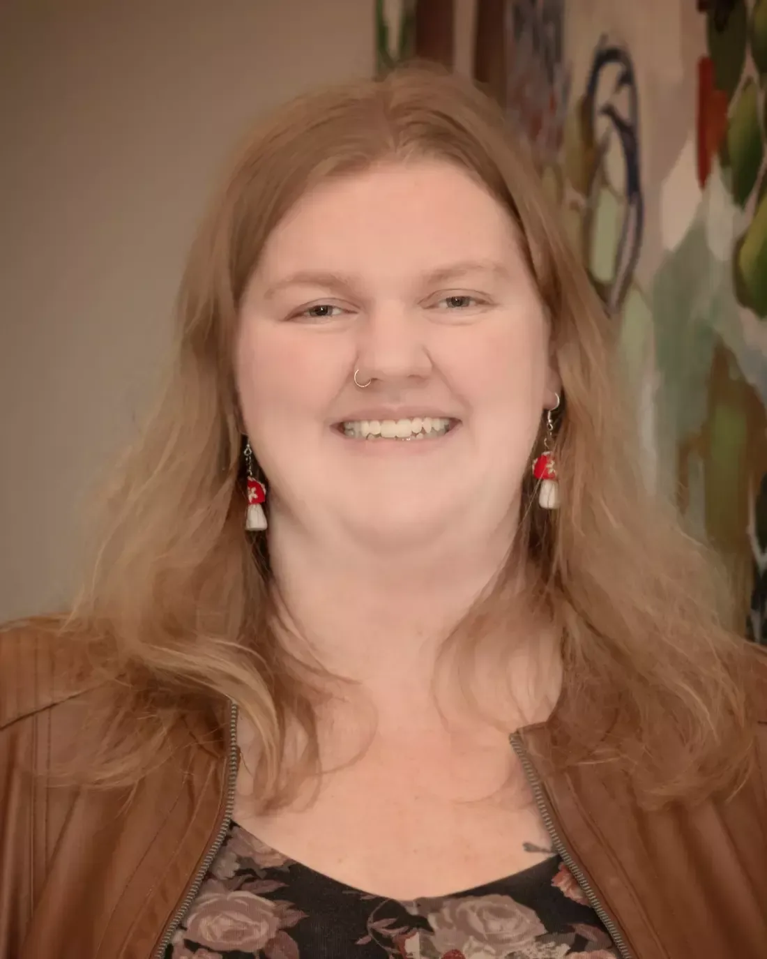 A woman wearing a brown jacket and earrings is smiling for the camera.