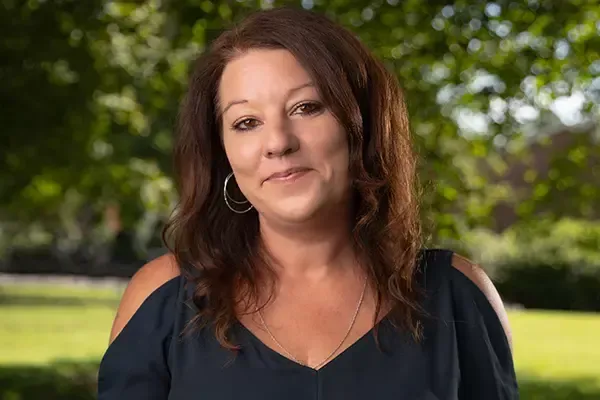 A woman is standing in front of a tree in a park.