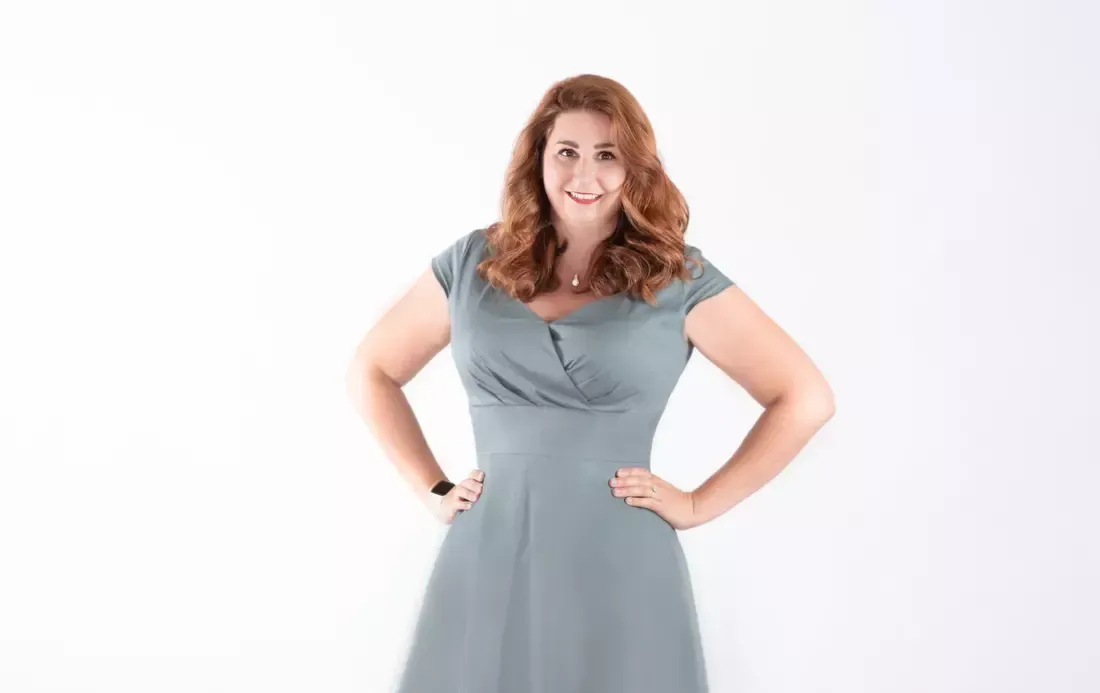 A woman in a blue dress is standing with her hands on her hips.