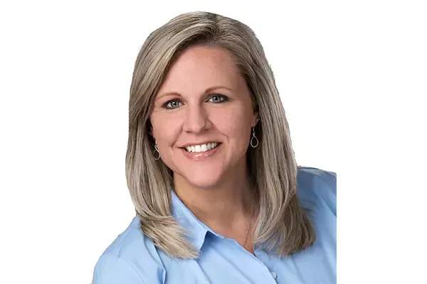 A woman wearing a blue shirt and earrings is smiling for the camera.