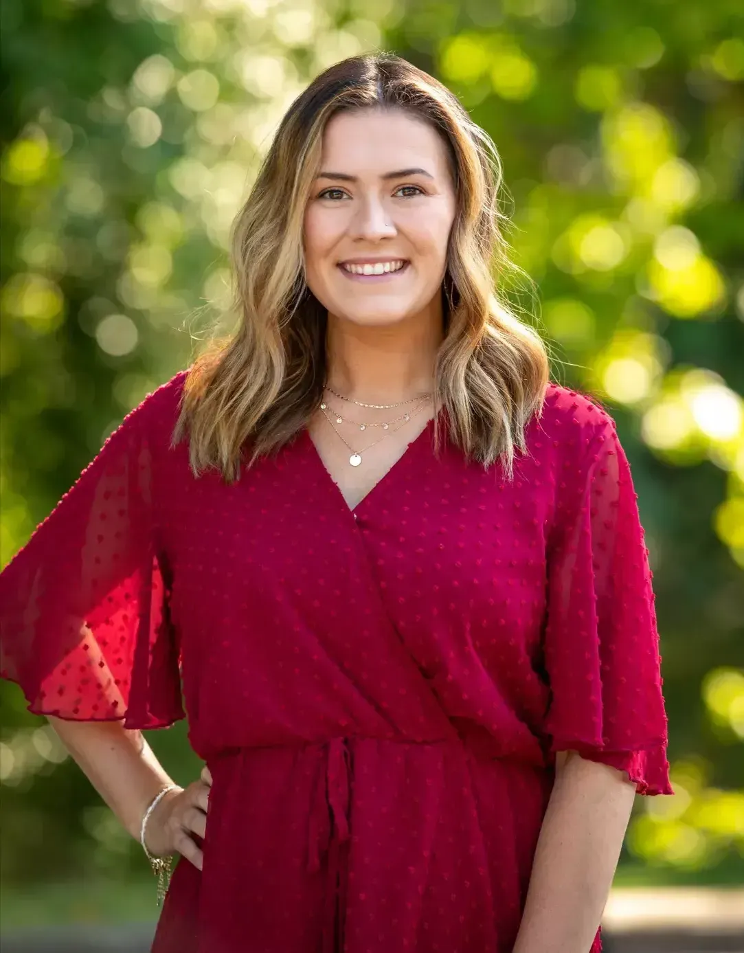 A woman in a red dress is standing with her hands on her hips and smiling.