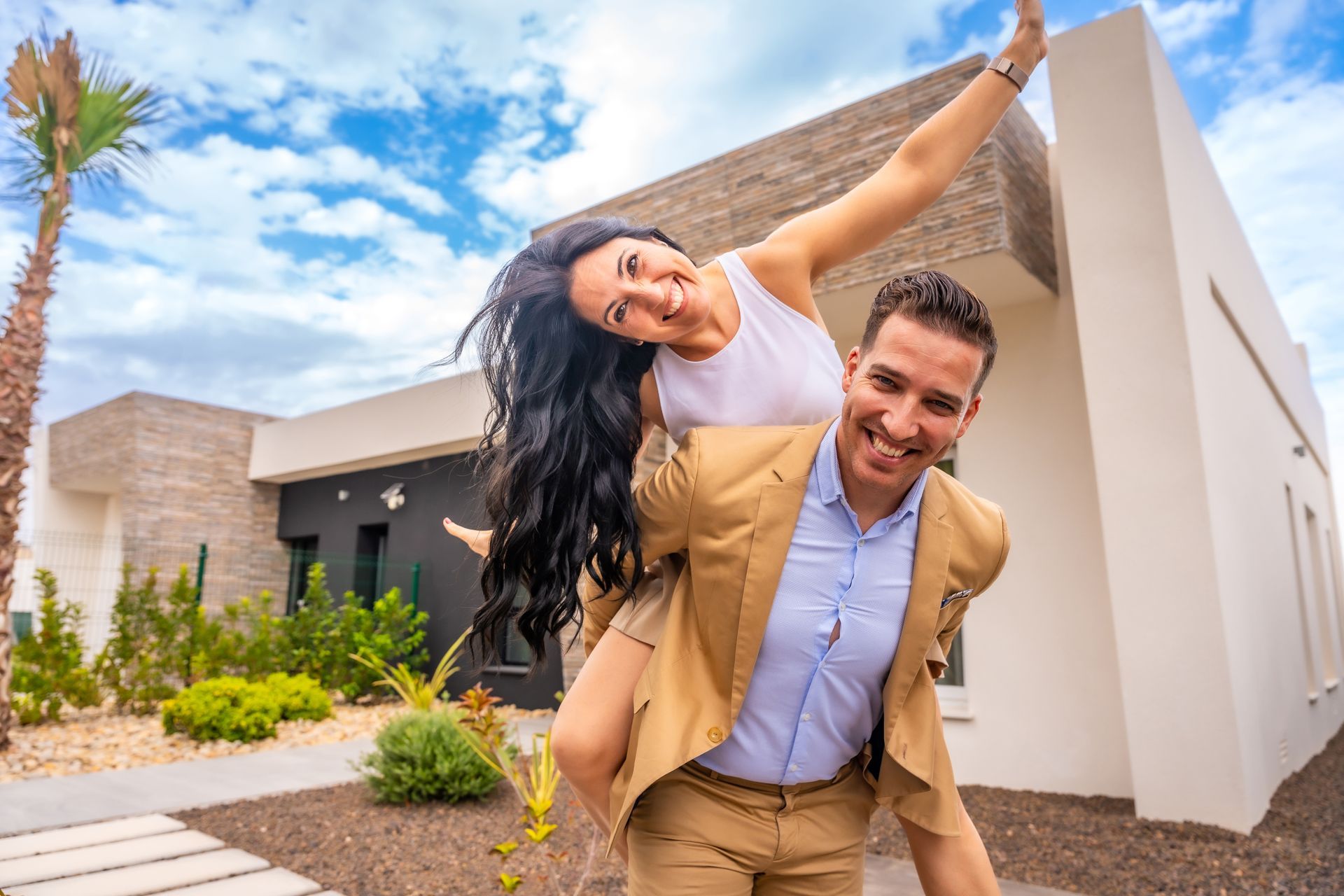 A man is carrying a woman on his shoulders in front of a house