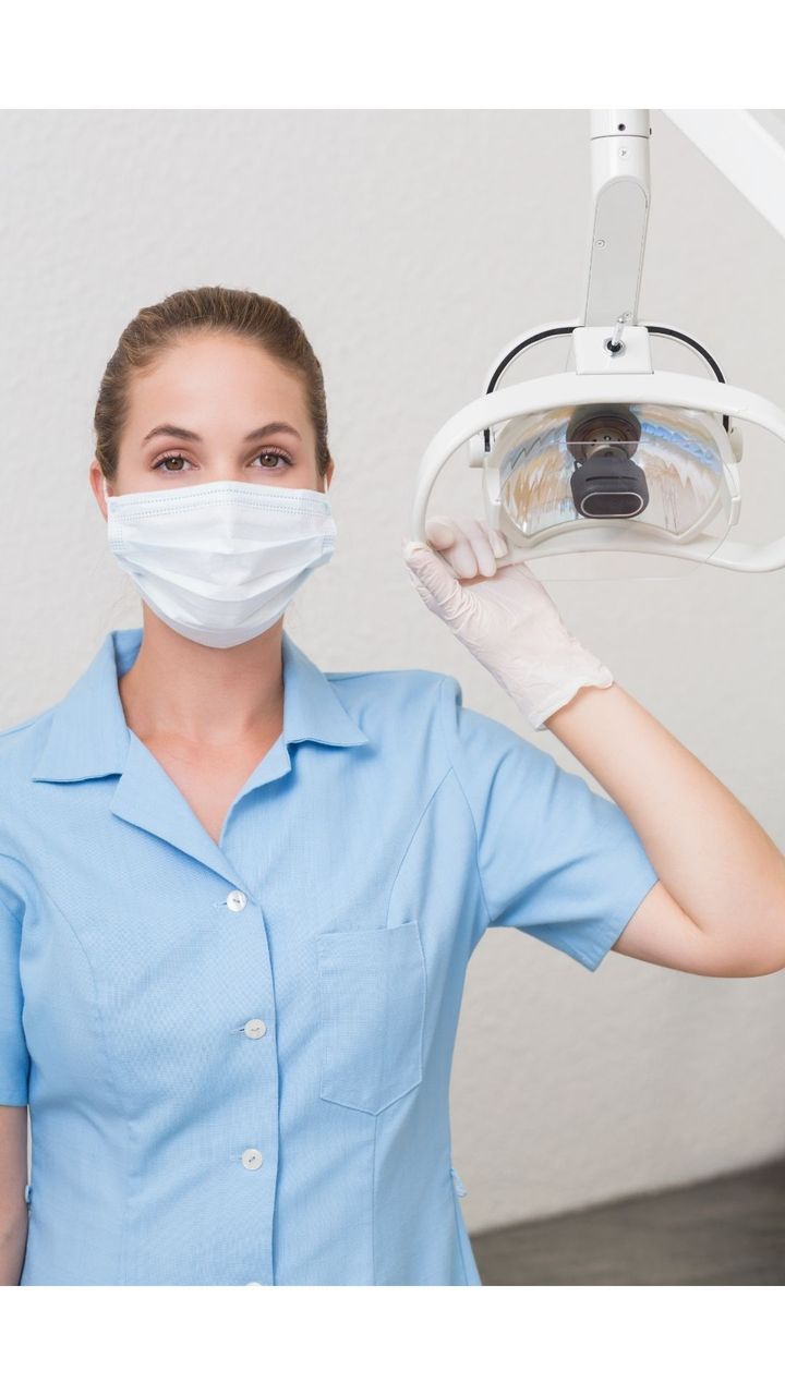 A female dentist wearing a mask and gloves is holding a light.