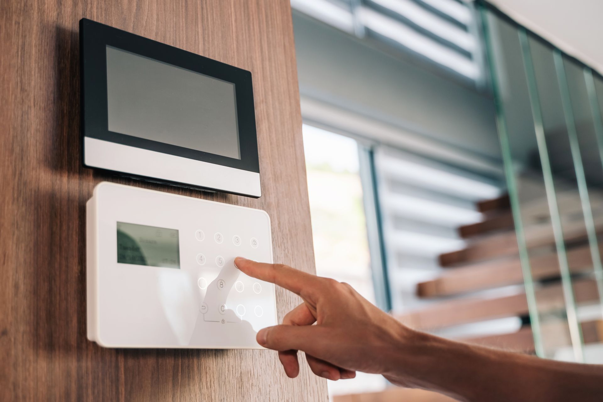 Person setting home security alarm on modern wall-mounted control panel.