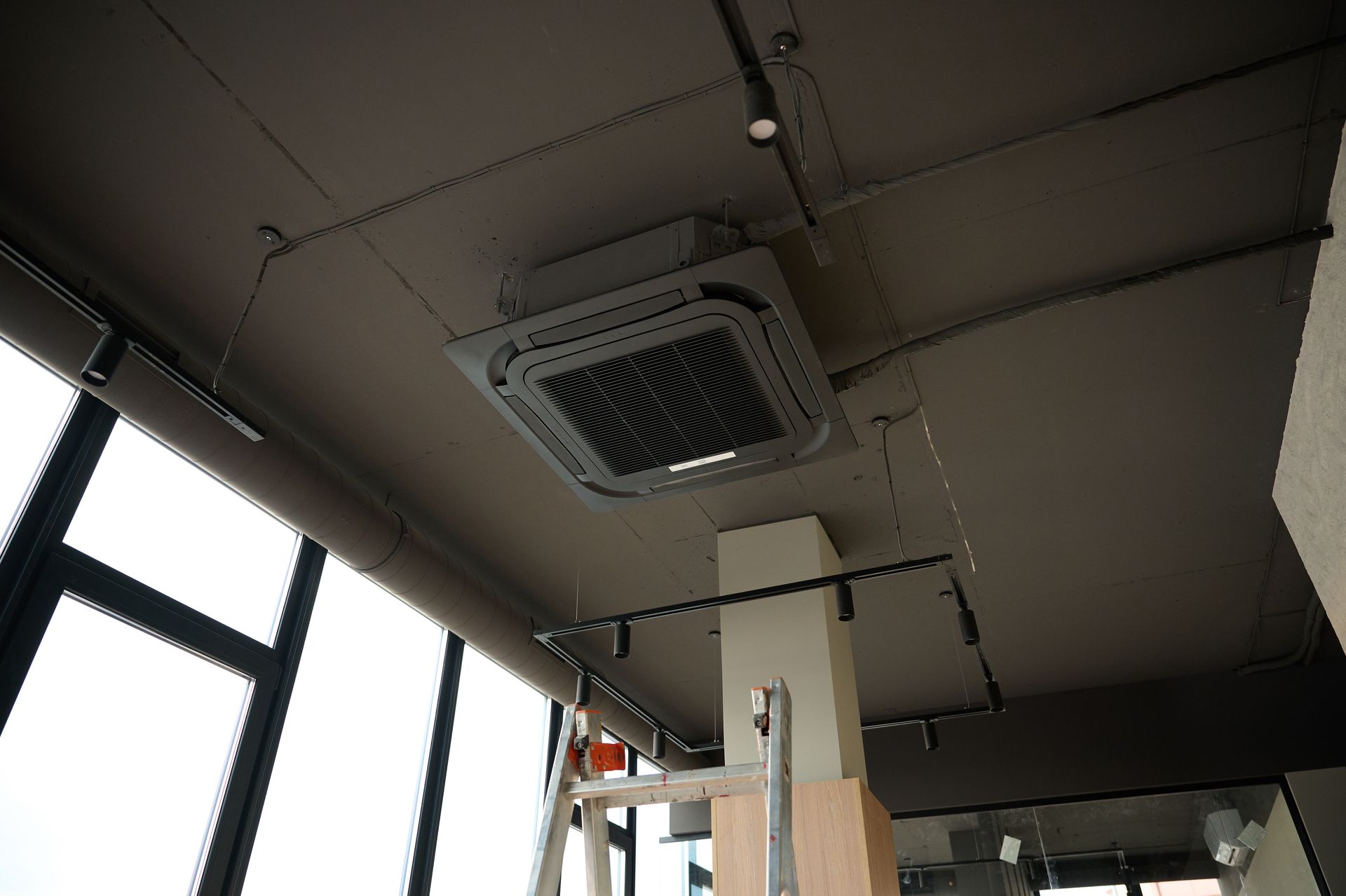 Ceiling-mounted HVAC unit installed in a commercial space with exposed ductwork and ladder below. Ceiling-mounted HVAC unit installed in a commercial space with exposed ductwork and ladder below.