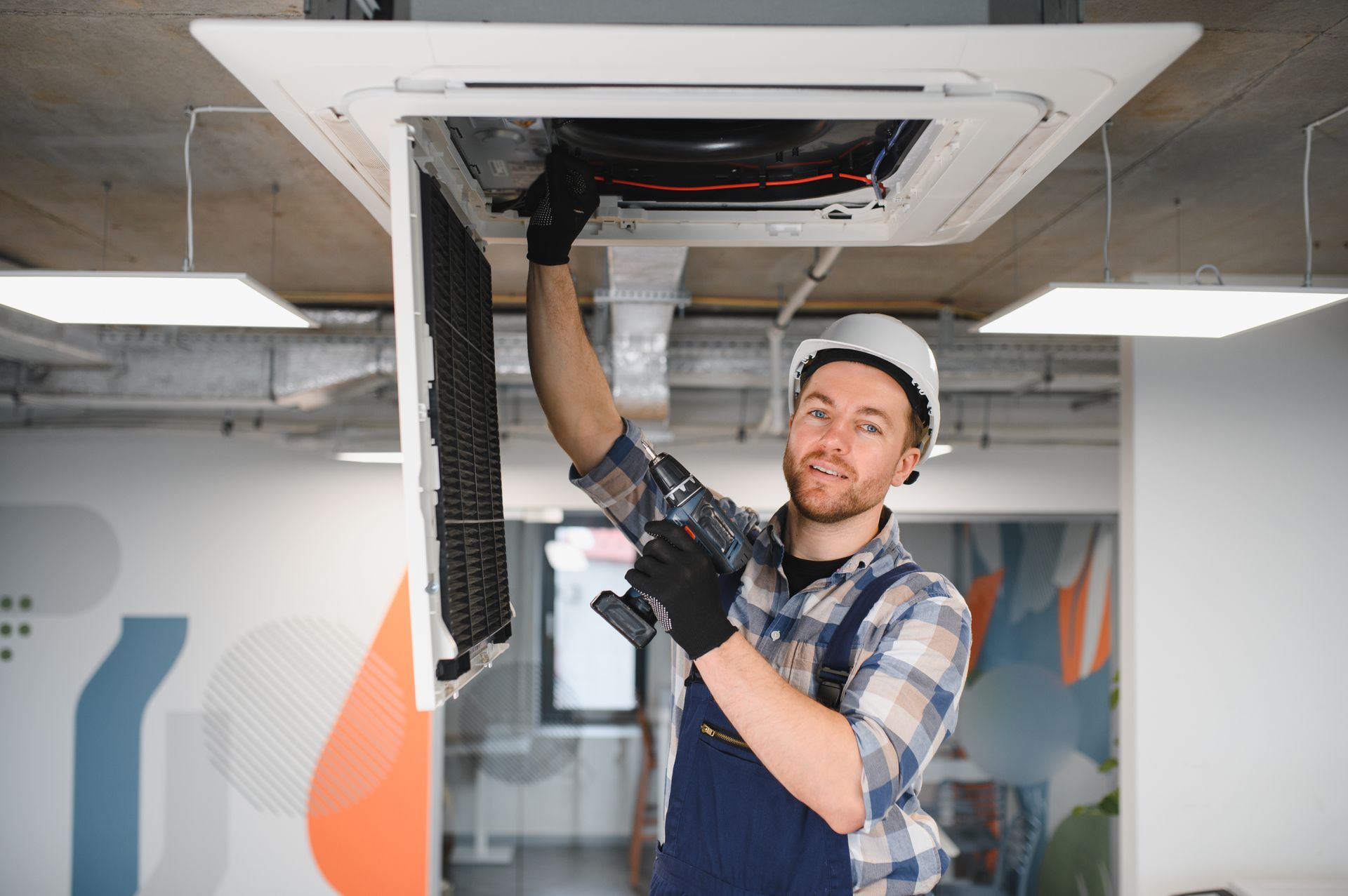 Technician services a ceiling-mounted HVAC unit inside a modern commercial building.