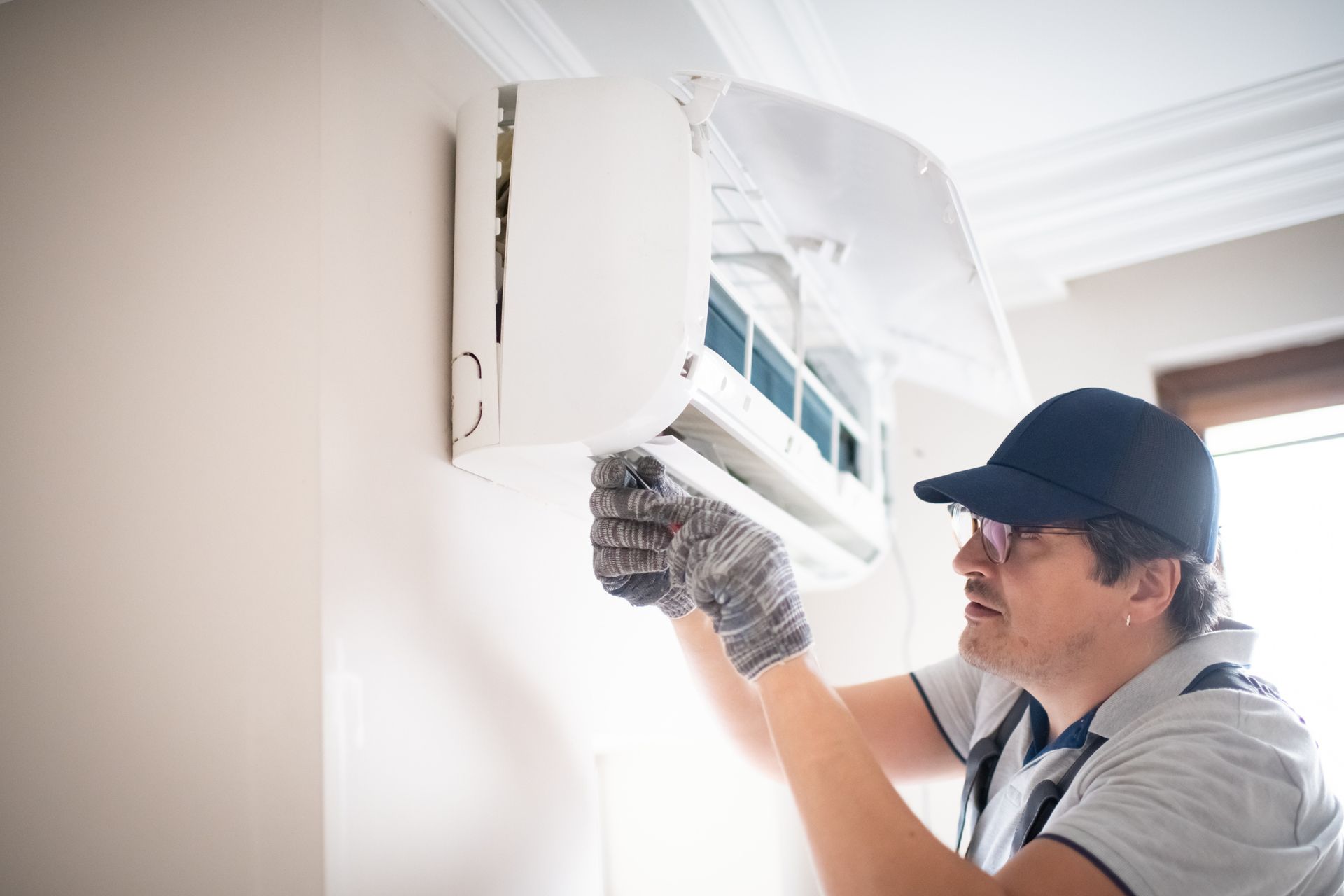 A technician wearing glasses performing air conditioner repair as part of a professional AC service.