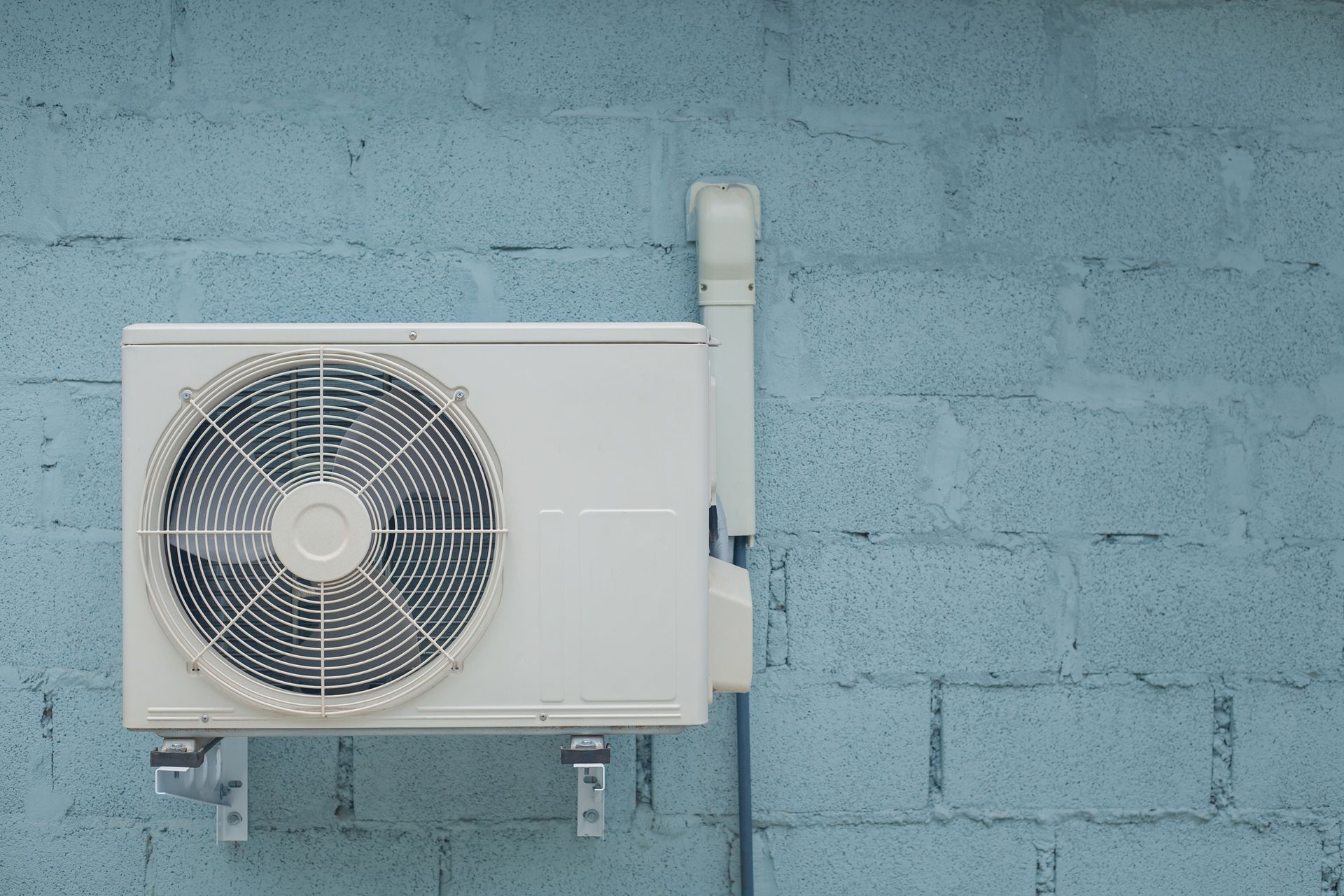 Outdoor air conditioner unit mounted on blue concrete wall for home cooling system.
