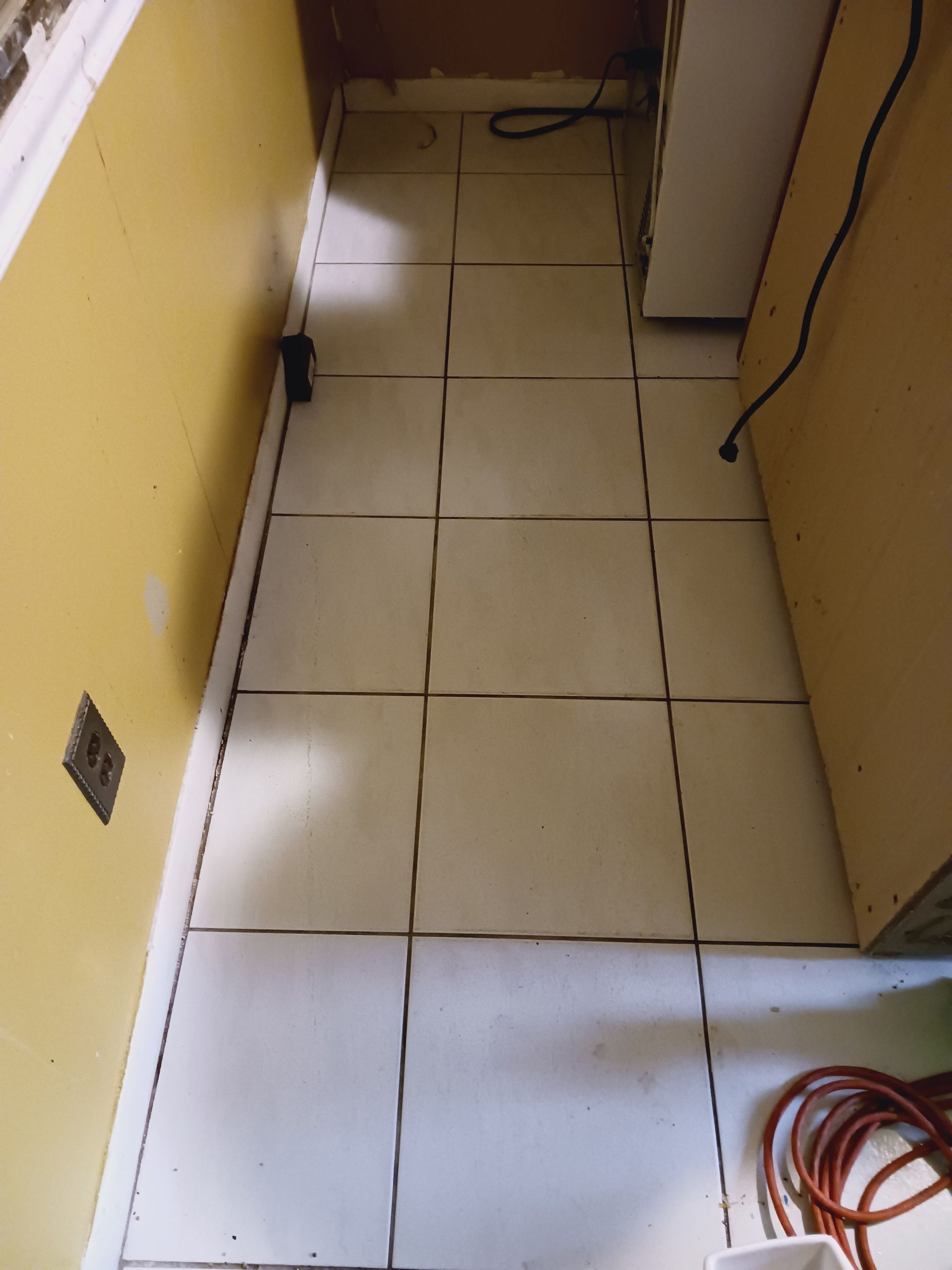 A white tiled floor in a room with a yellow wall