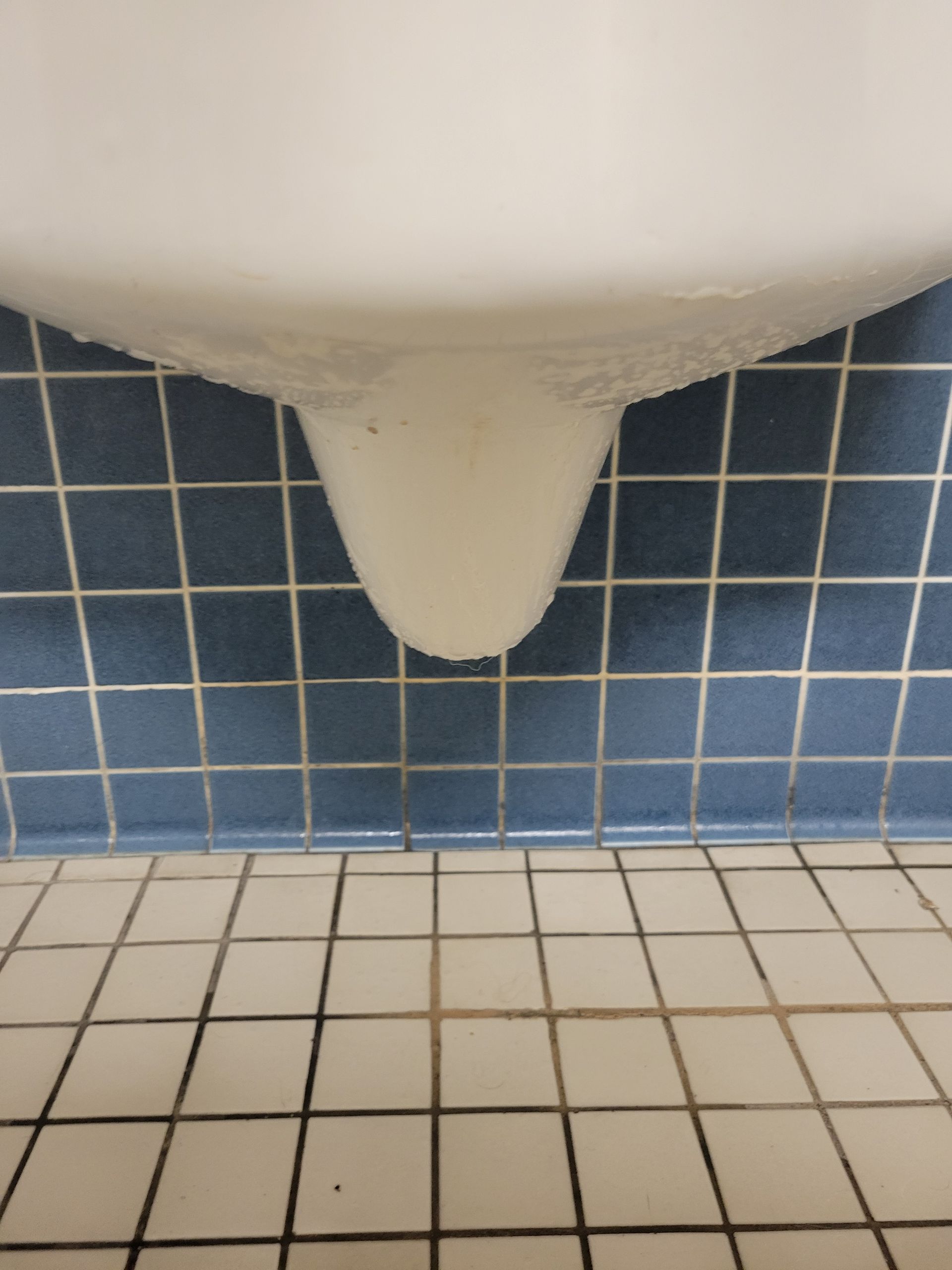 A white urinal against a blue tiled wall