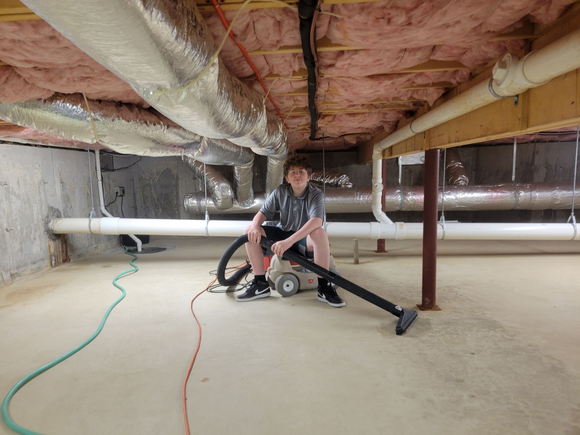 A man is sitting on a vacuum cleaner in a basement.