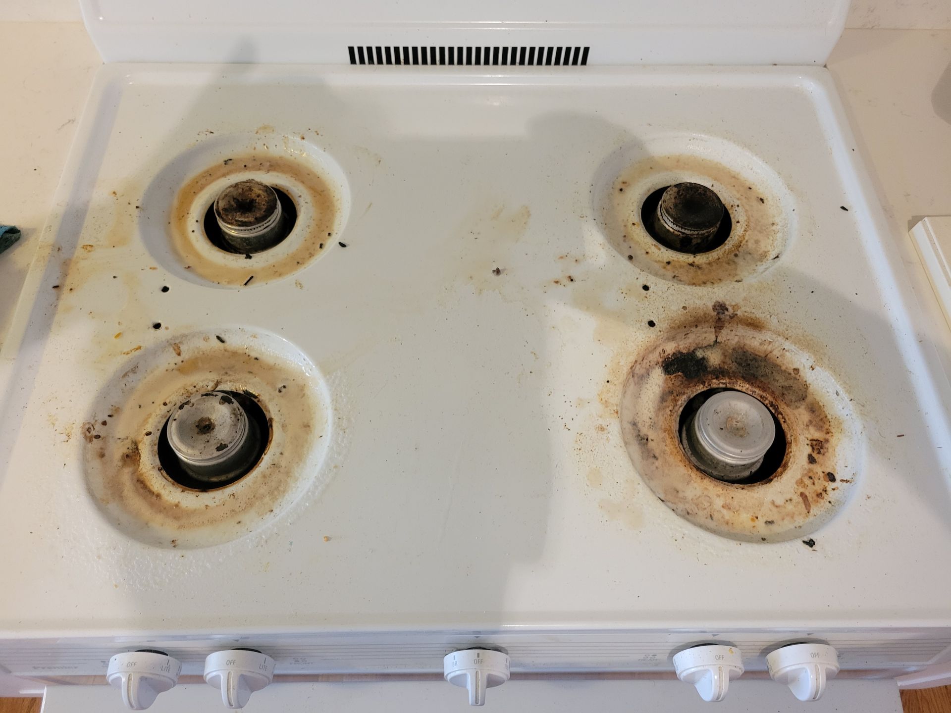 A dirty white stove top with four burners.
