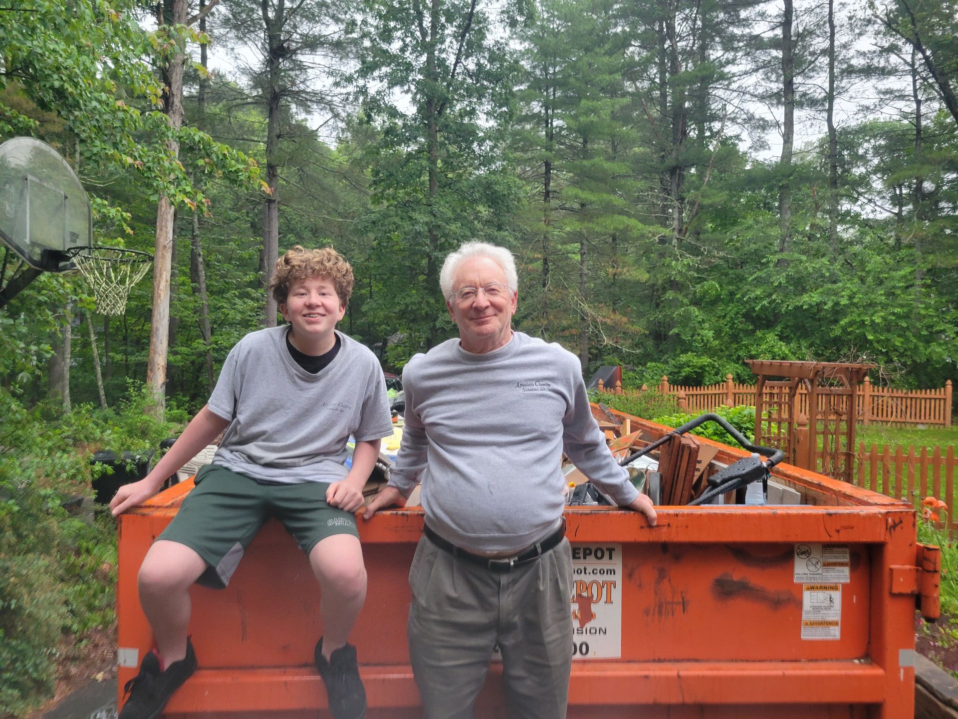 A man and a boy are sitting on top of an orange dumpster.