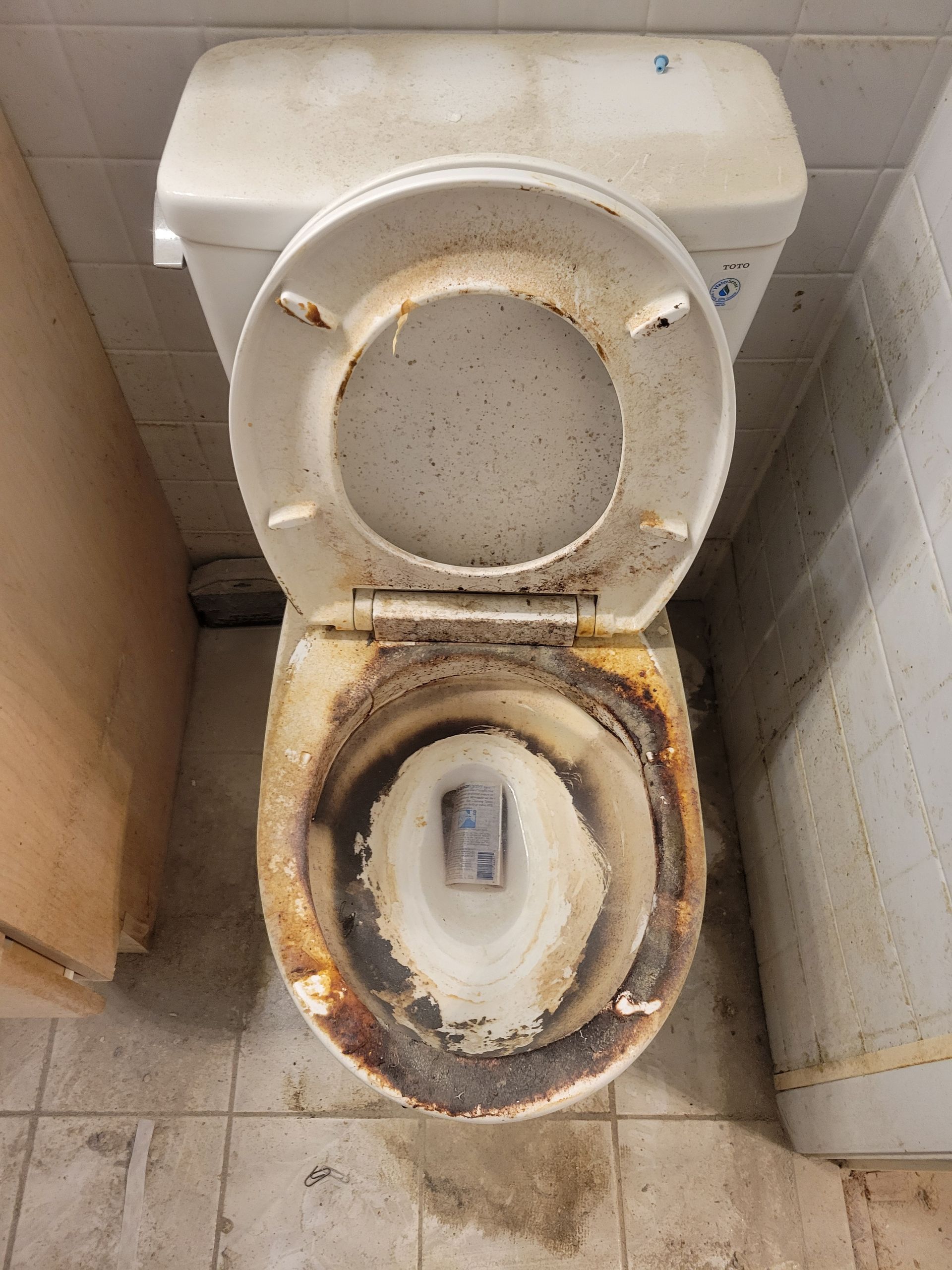 A dirty toilet is sitting on a tiled floor in a bathroom.