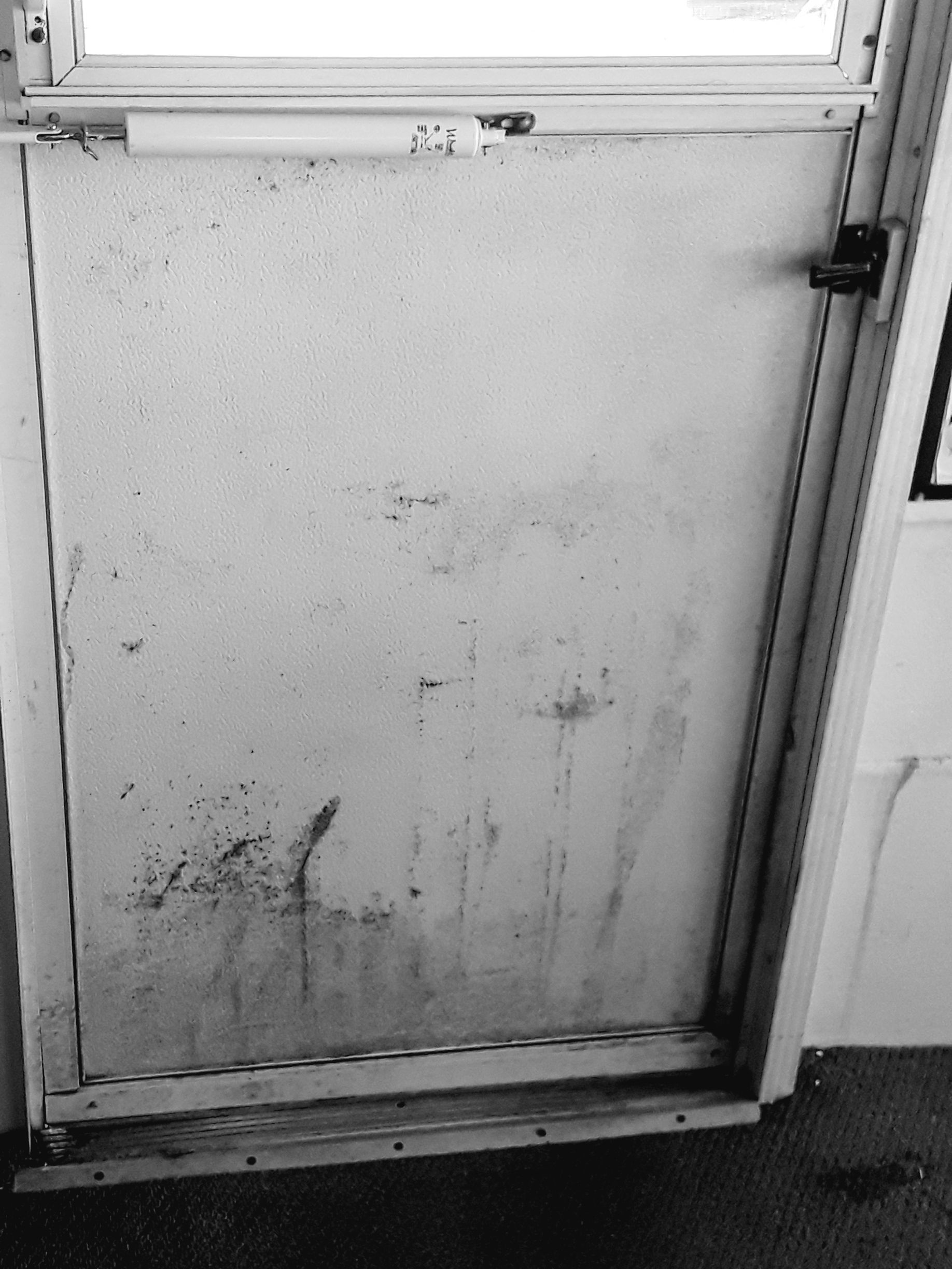 A black and white photo of a dirty door with a window.
