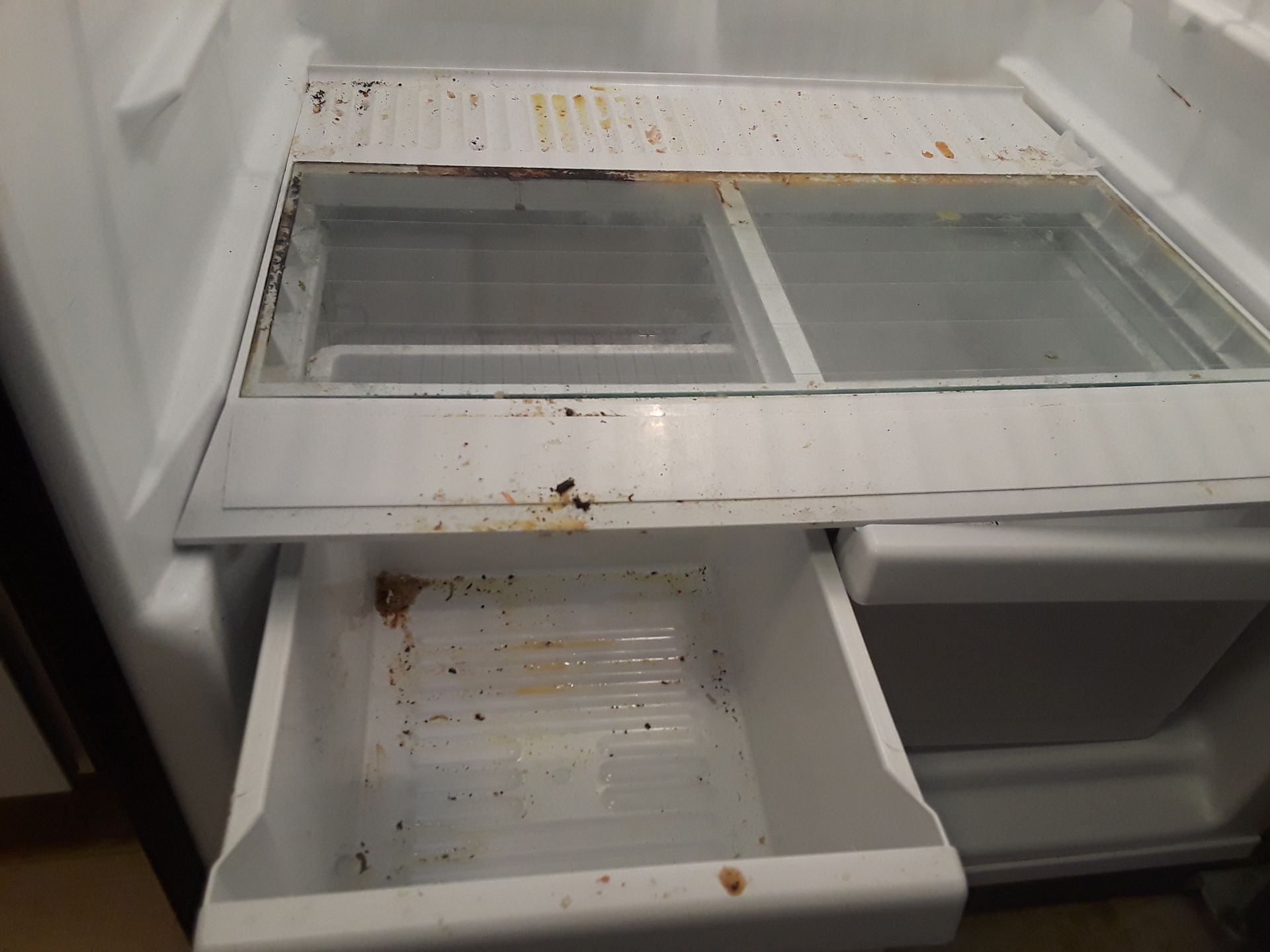The inside of a dirty refrigerator with a drawer open.