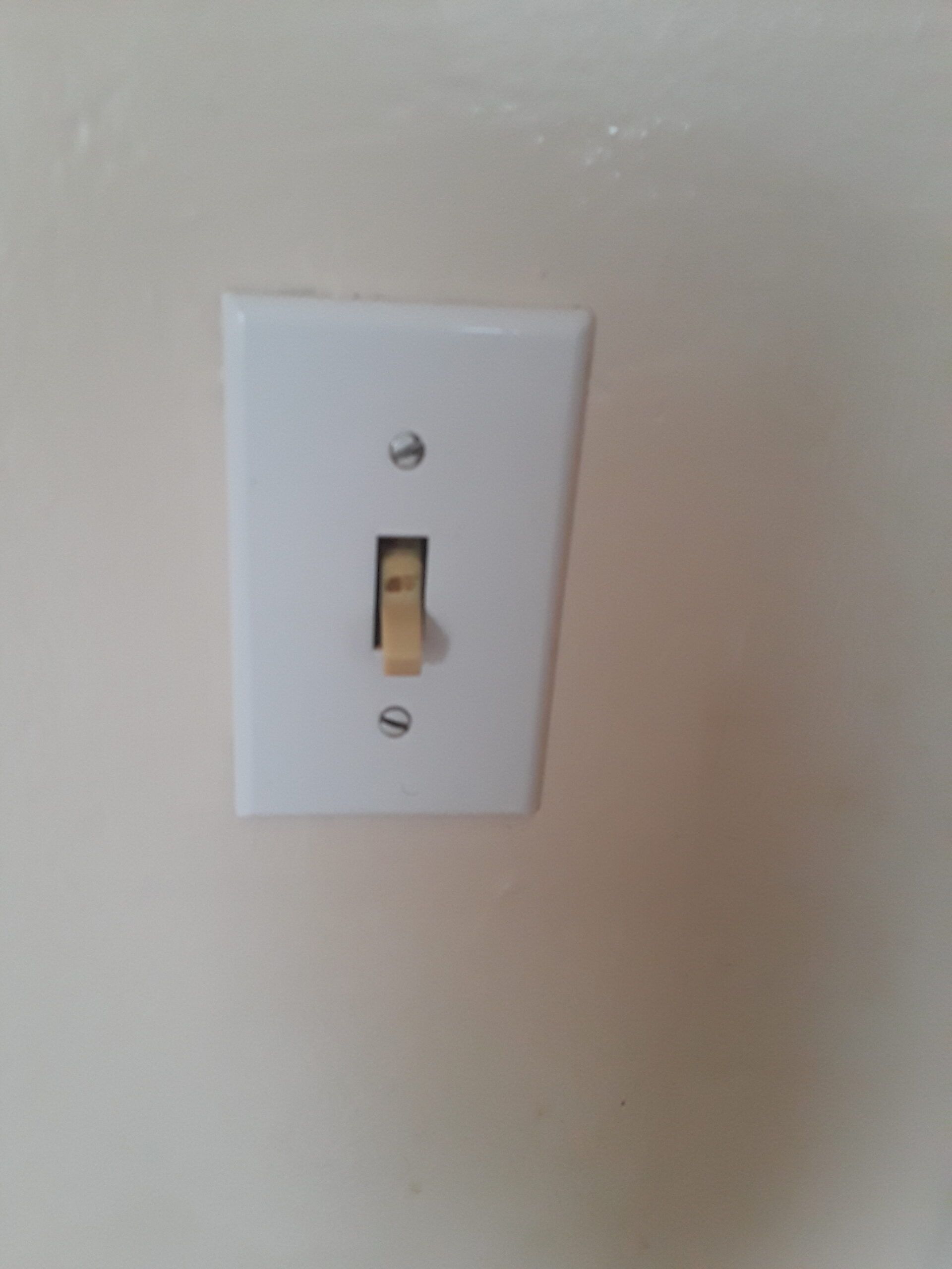 A light switch is hanging on a white wall.