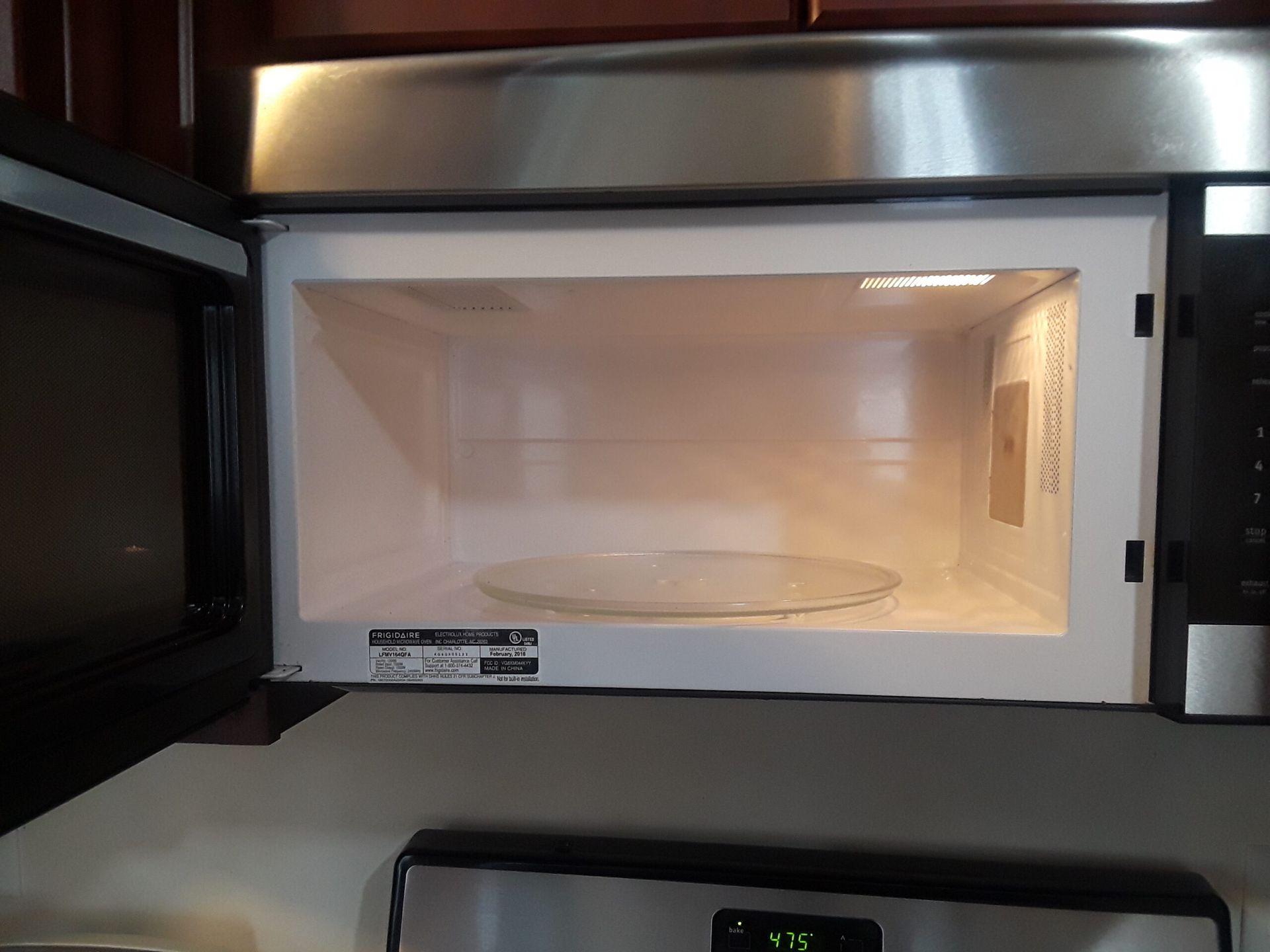 An empty microwave oven with the door open and a digital clock on the stove.