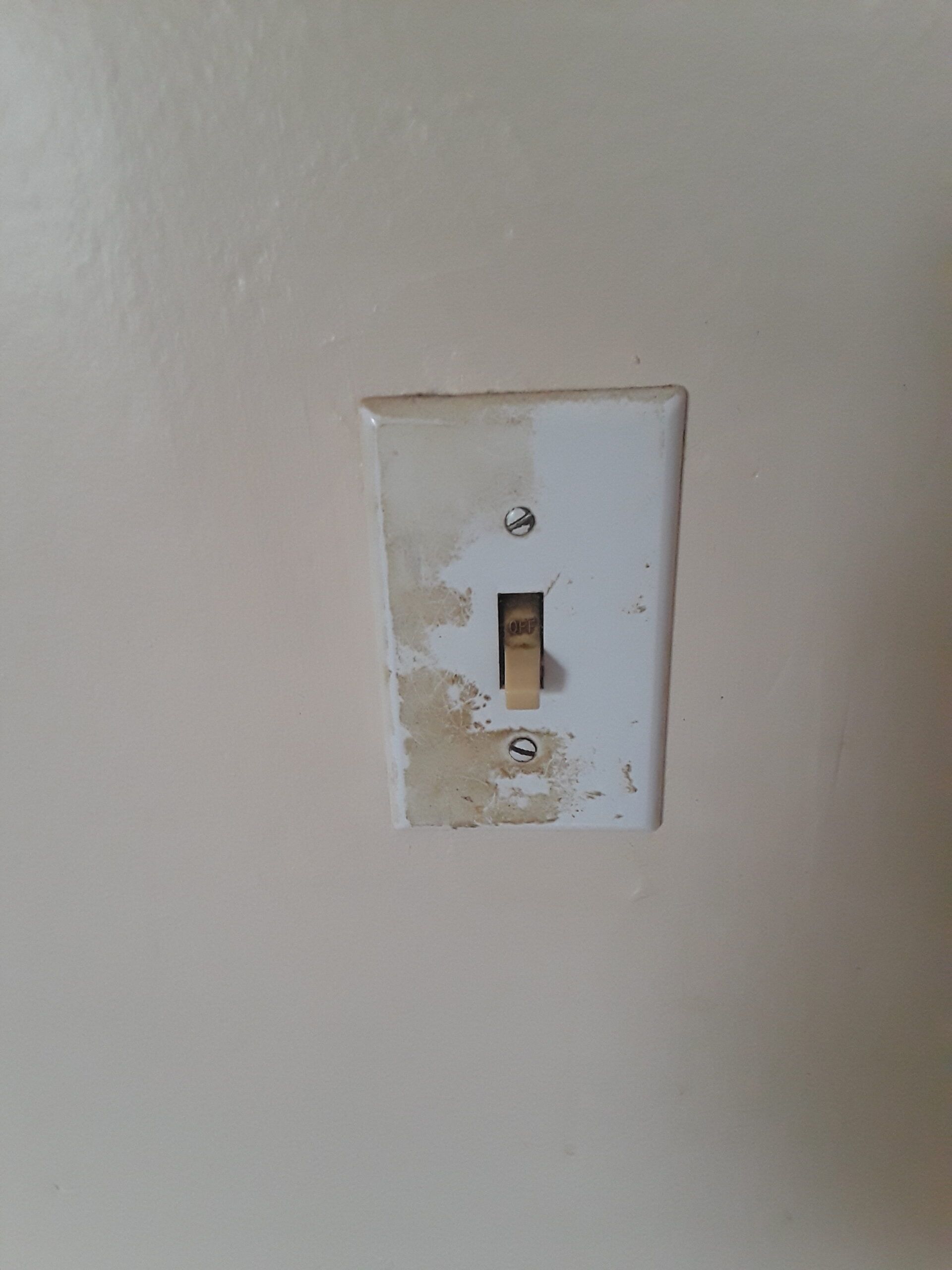 A light switch on a wall with peeling paint.