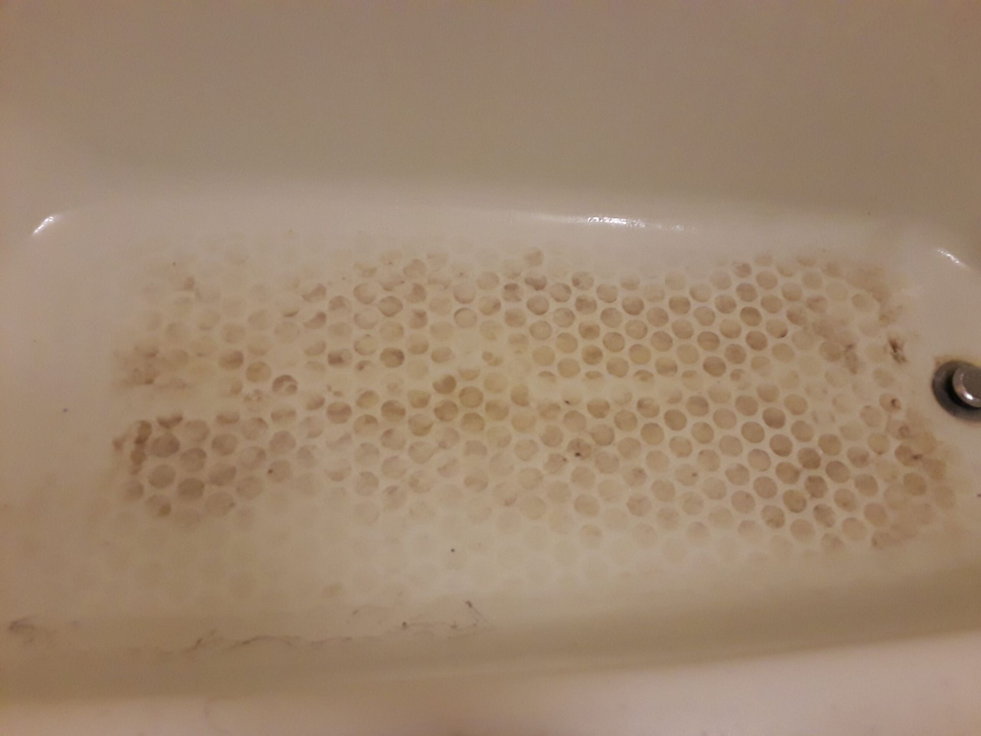 A dirty bathtub with a honeycomb pattern on the floor.