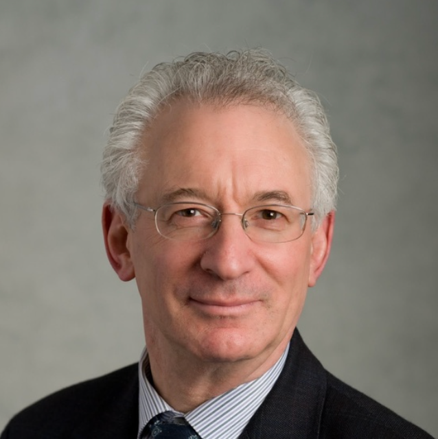 A man wearing glasses and a suit is smiling for the camera