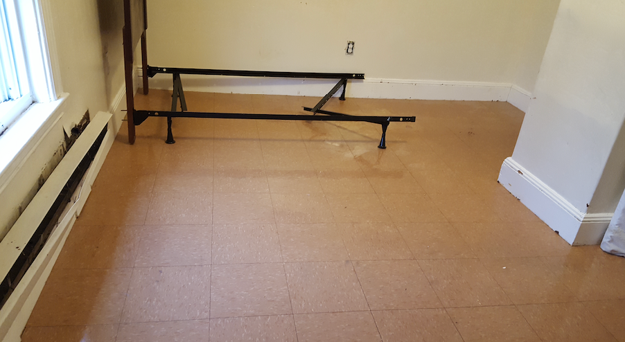 A bed frame is sitting on the floor of a room next to a window.