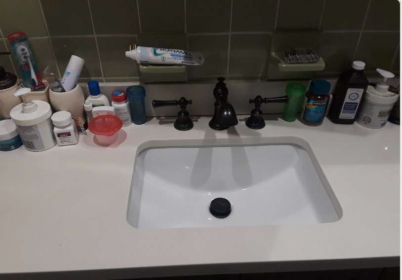 A bathroom counter with a sink , toothpaste , soap , and other items.