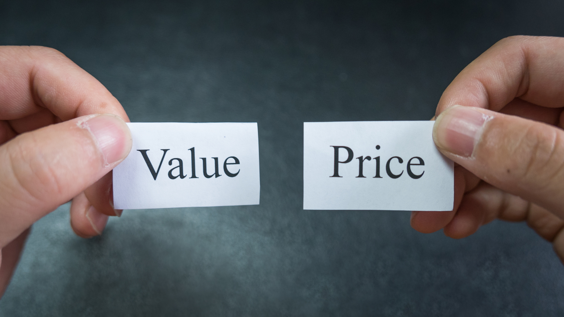 A person is holding two pieces of paper that say value and price.