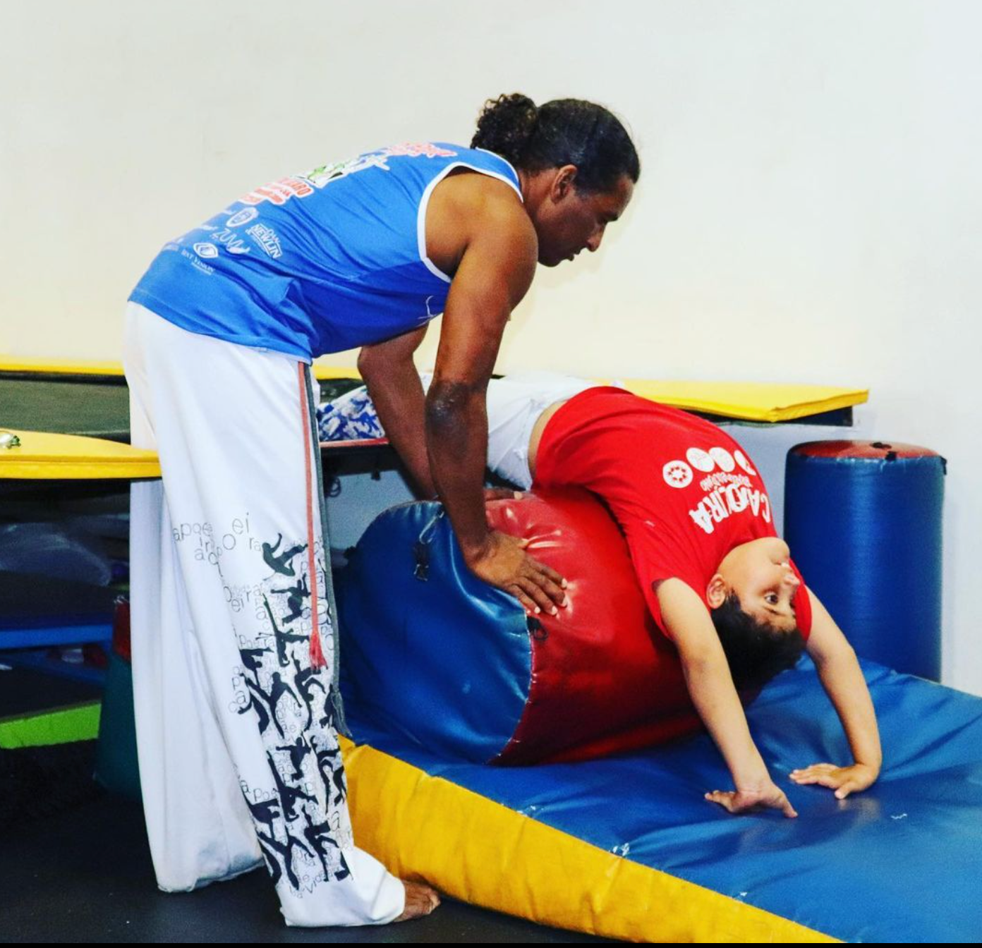 a man in a blue tank top is helping a child do a handstand
