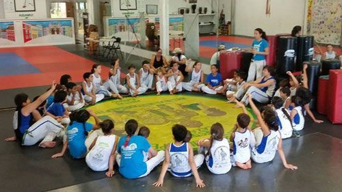 a group of children are sitting in a circle on the floor in a gym .
