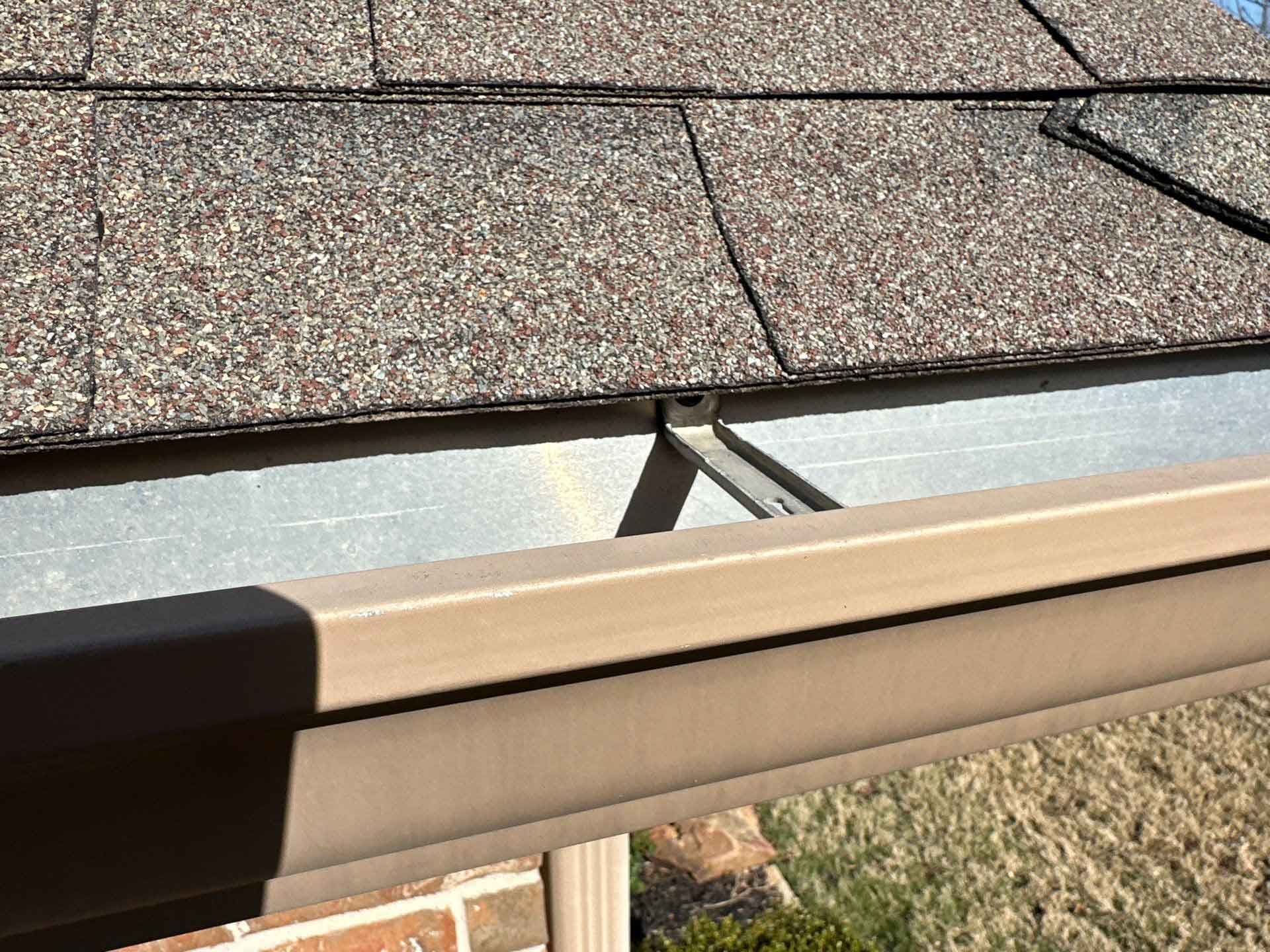 A close up of a gutter on a roof with shingles.