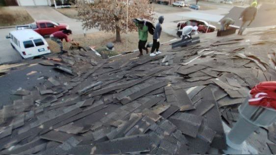 Workers removing shingles from a damaged roof on a house